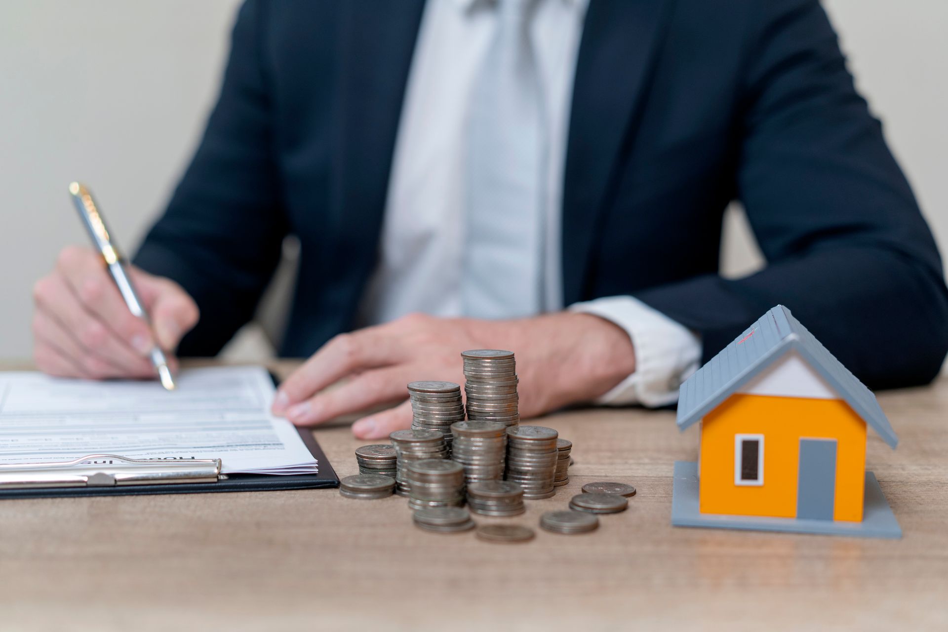 A wills lawyer signing estate documents besides coins and a house model.