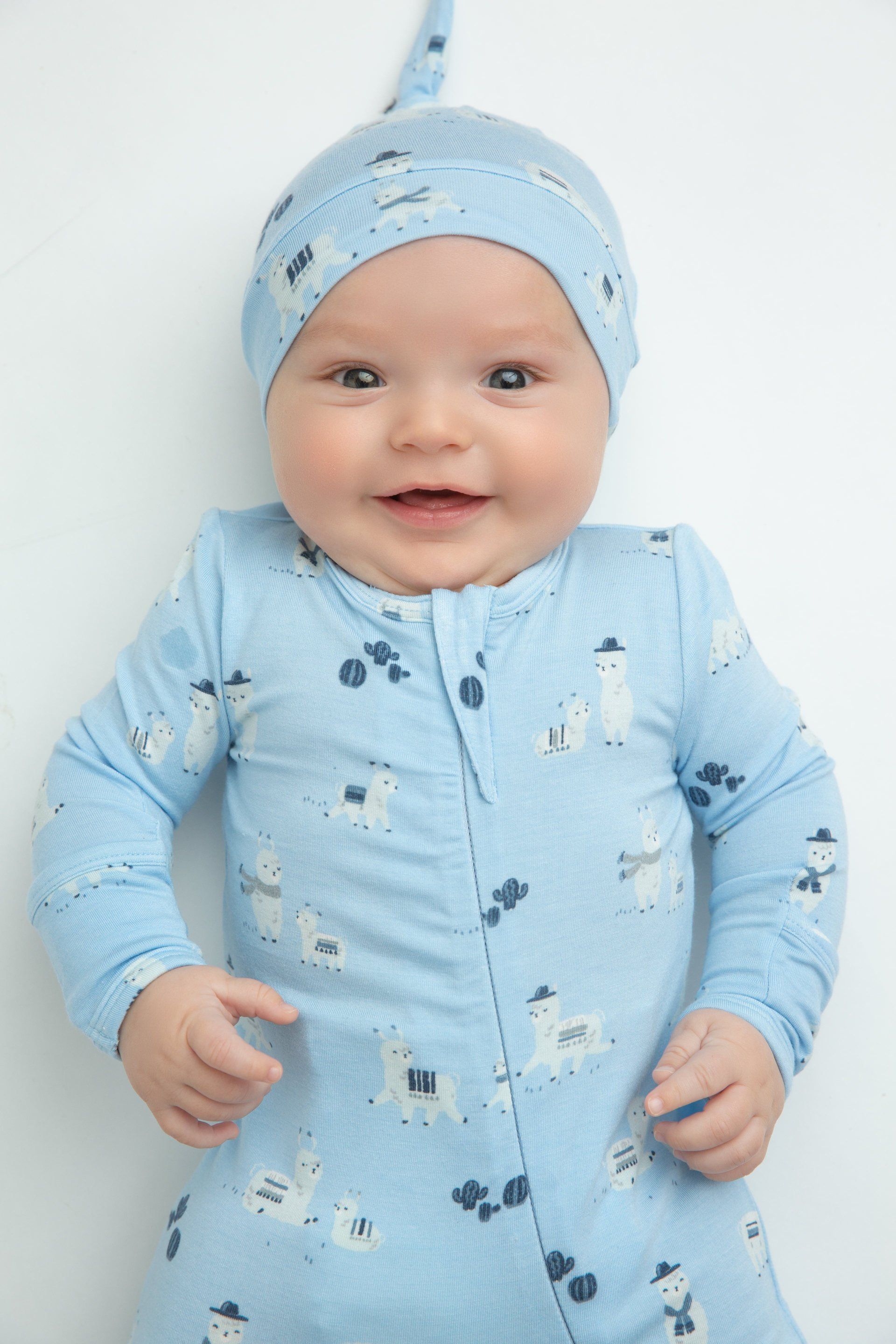 A baby wearing a blue outfit and a hat is smiling.