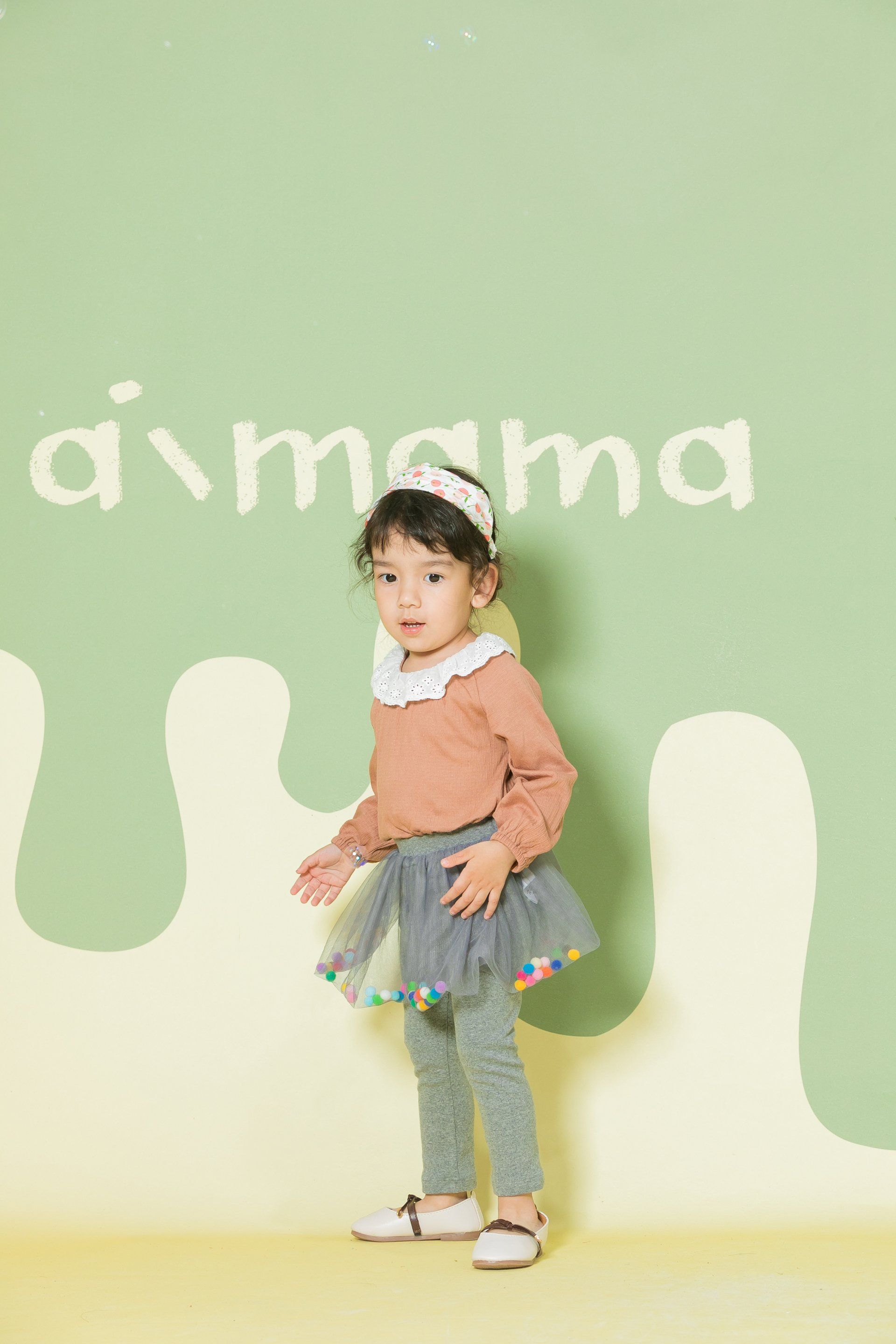 A little girl is standing in front of a green wall.