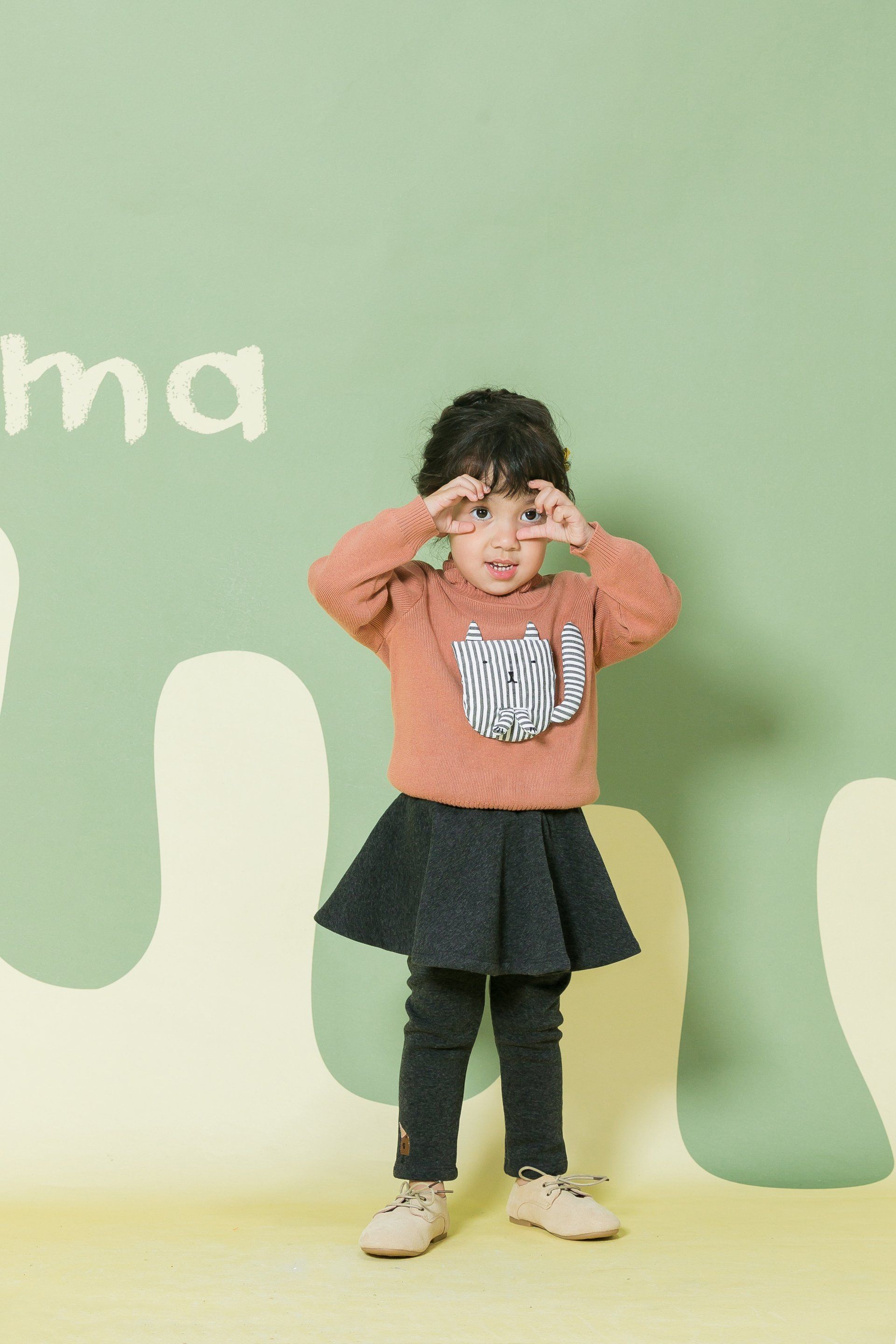A little girl is standing in front of a green wall.