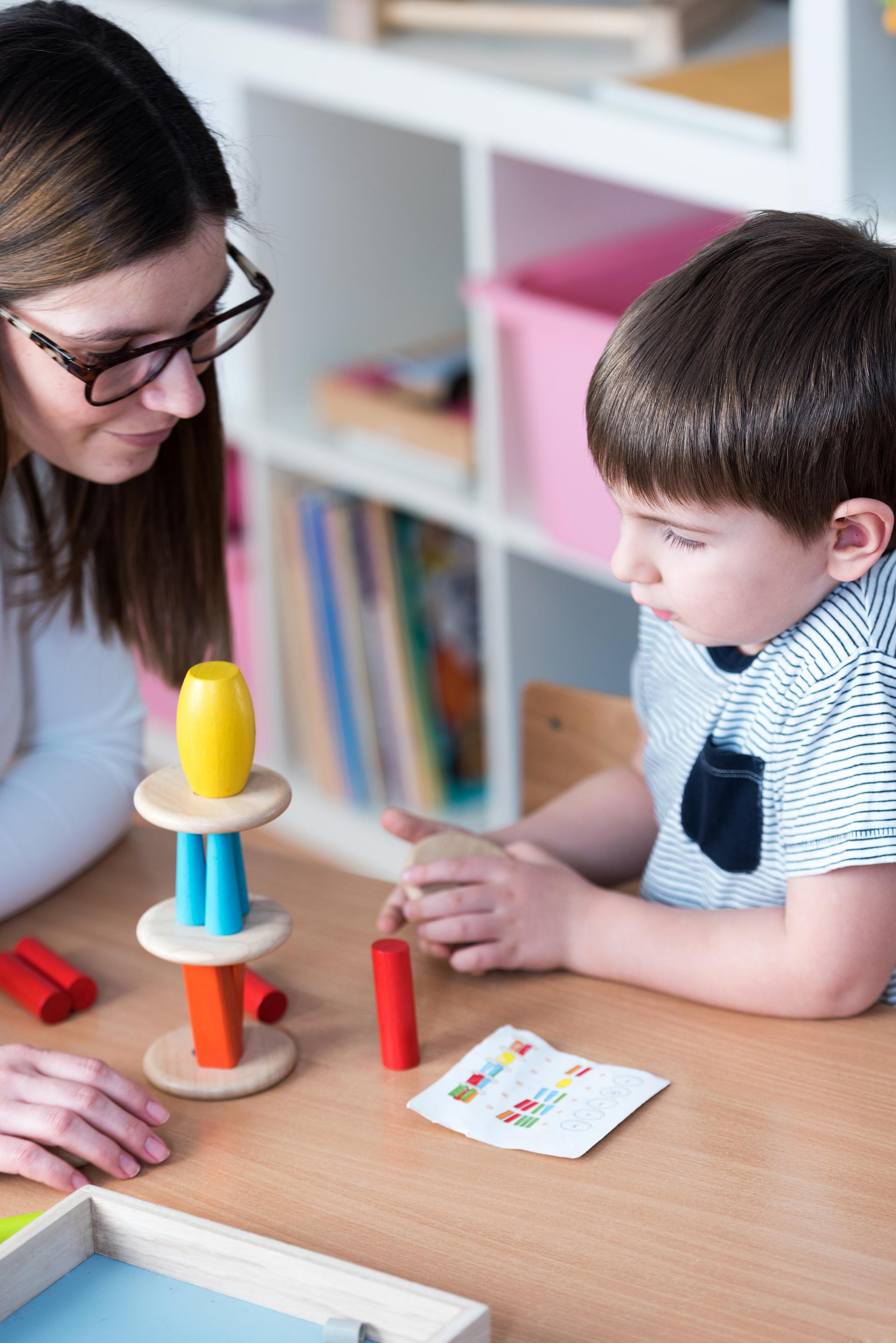 A woman and a child are playing with toys at a table.