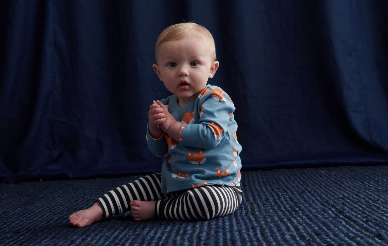A baby is sitting on the floor in front of a blue curtain.
