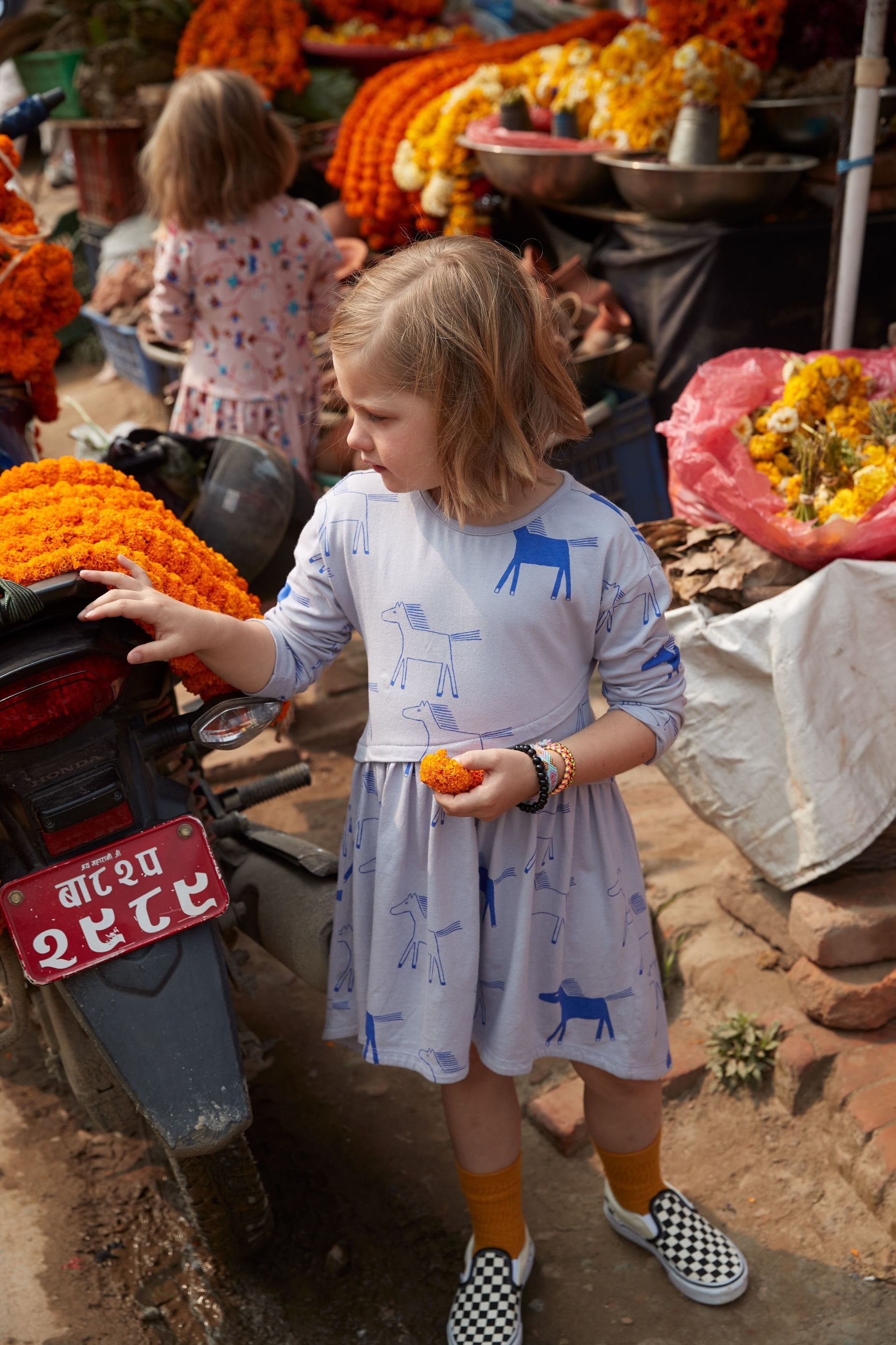 A little girl is standing in front of a motorcycle holding an orange.