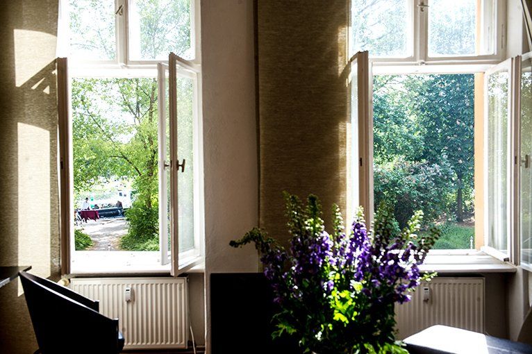 Eine Vase mit lila Blumen steht vor einem Fenster in einem Wohnzimmer.