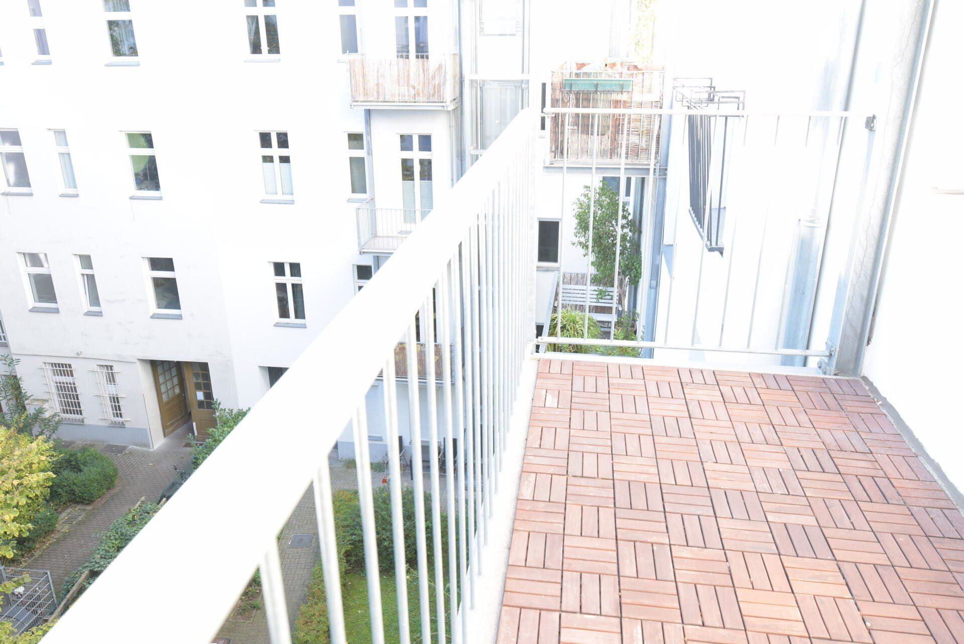 Ein Balkon mit weißem Geländer und Ziegelboden vor einem Gebäude.