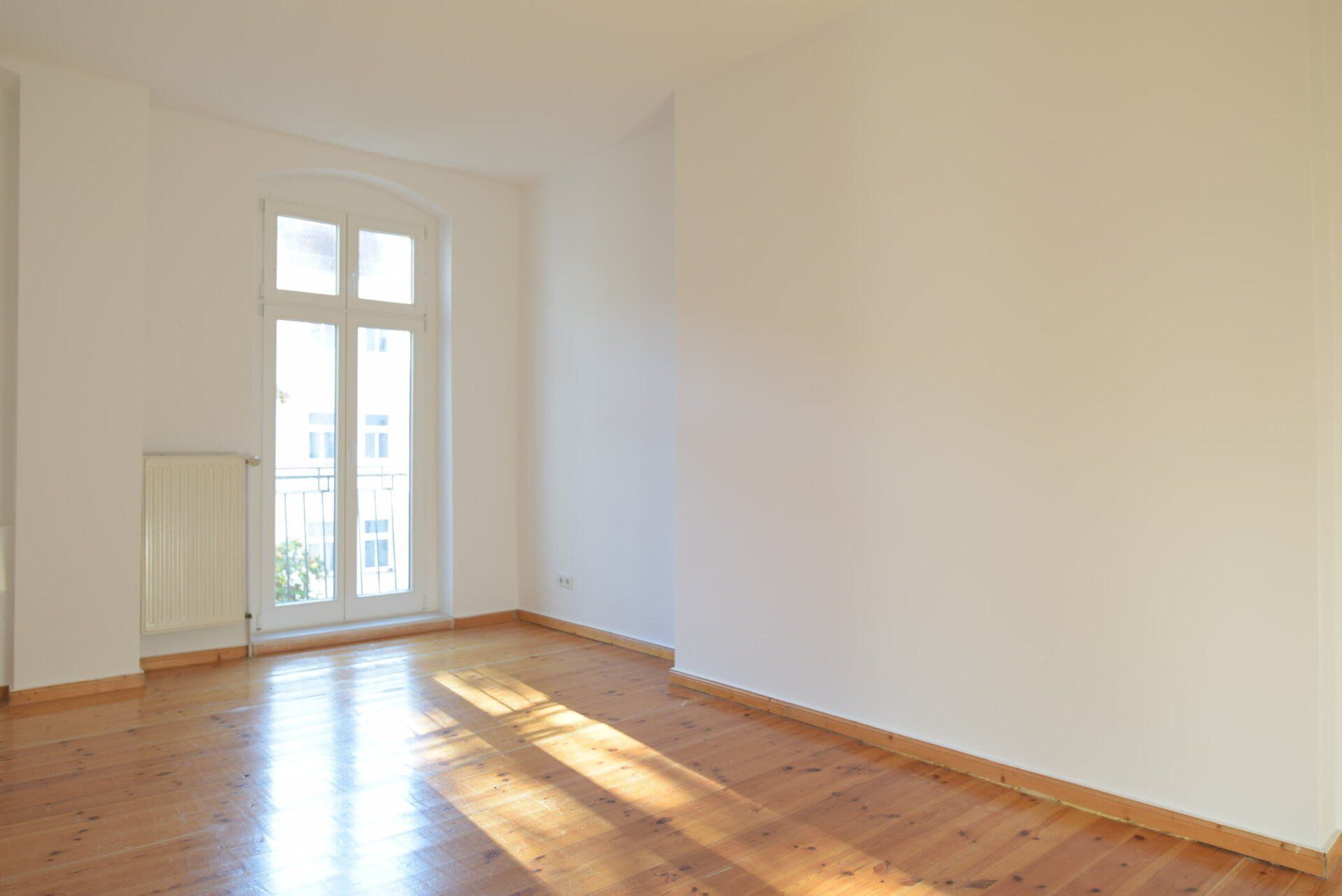 Ein leerer Raum mit Holzboden und weißen Wänden.