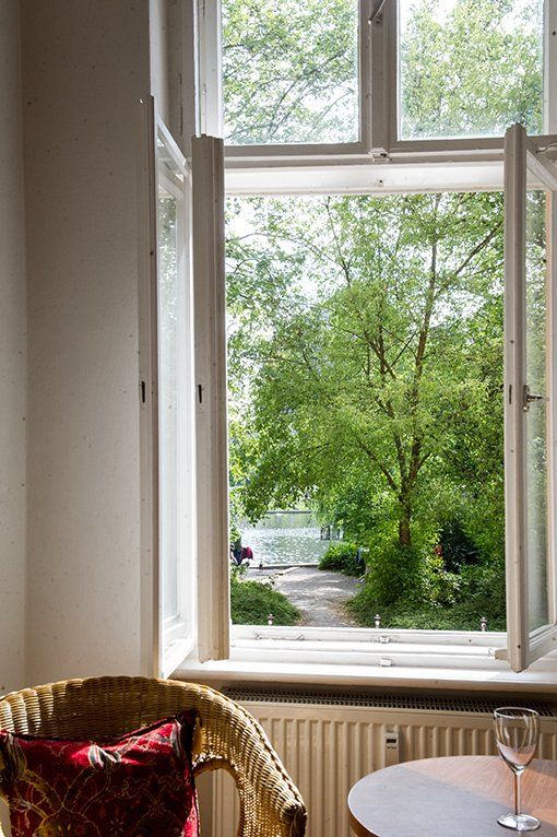 Vor einem Fenster mit Blick auf Bäume stehen ein Stuhl und ein Tisch.