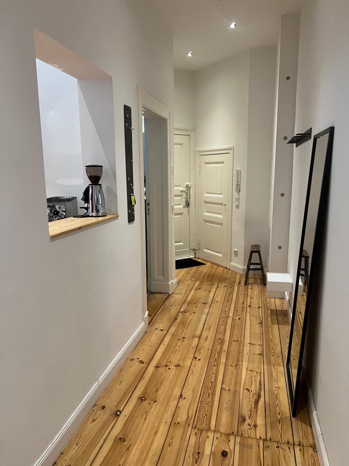 Ein Flur mit Holzboden und einem Spiegel an der Wand.
