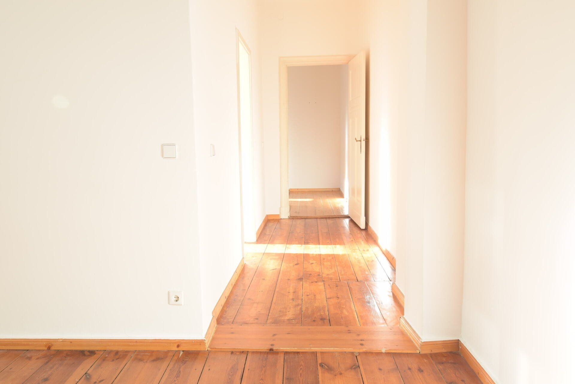 Ein leerer Flur mit Holzboden und weißen Wänden.