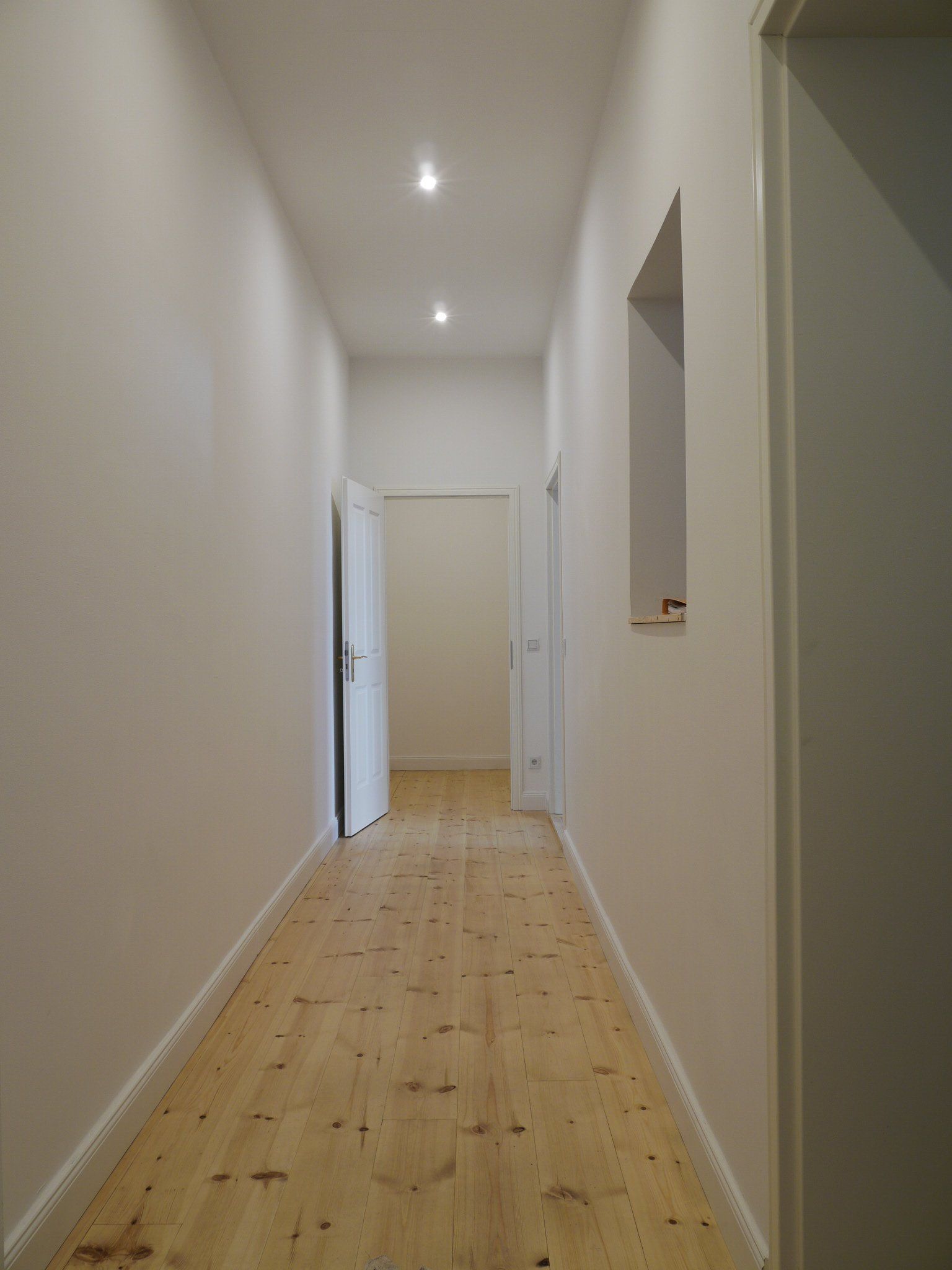 Ein langer Flur mit Holzböden und weißen Wänden