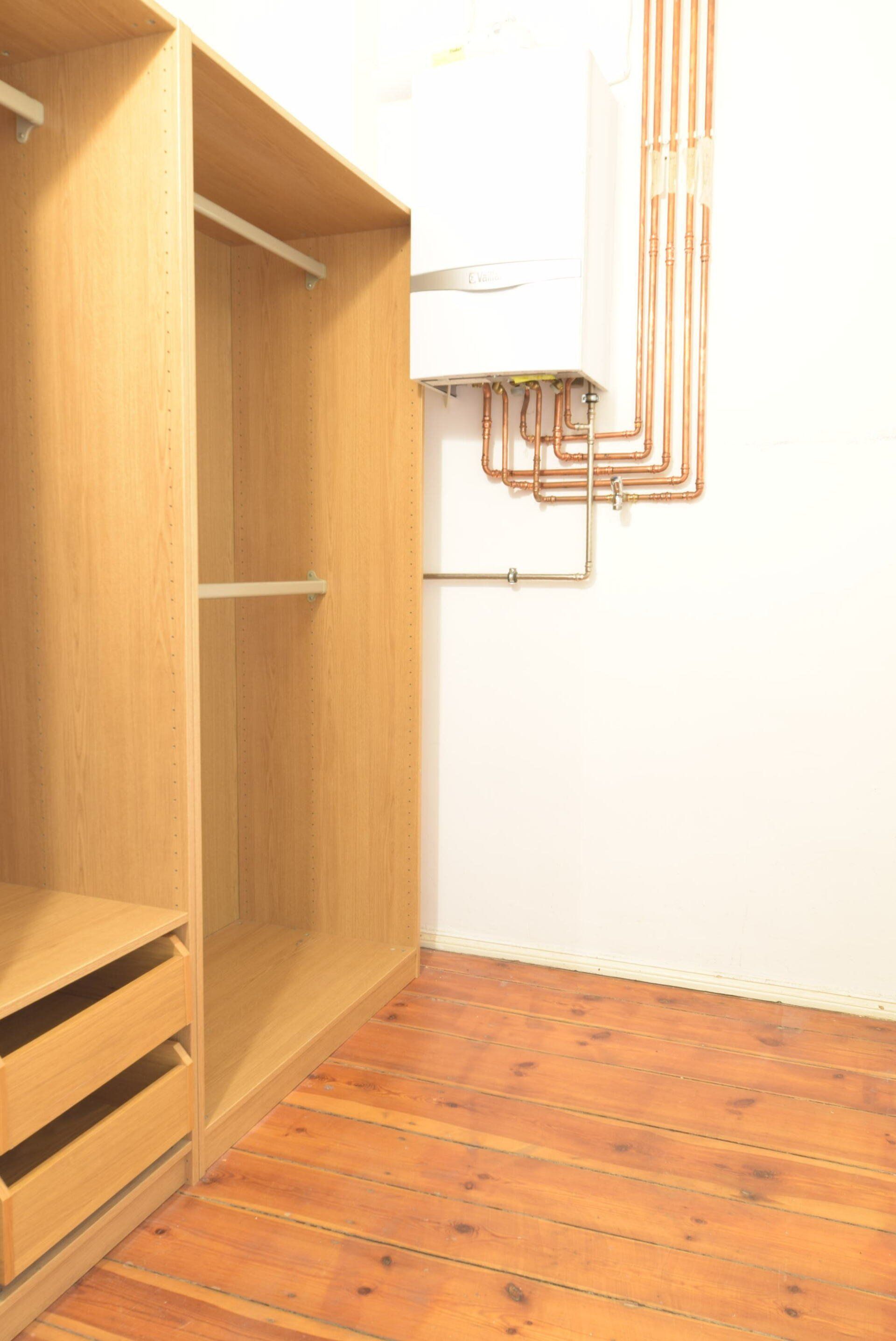 Ein begehbarer Kleiderschrank mit Holzschränken und Kupferrohren an der Wand.