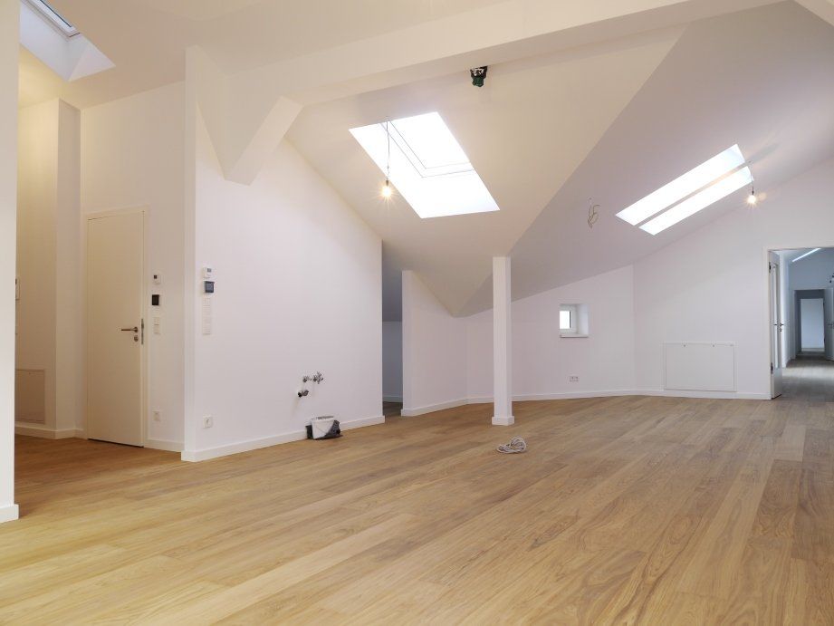 Ein großer, leerer Raum mit Holzboden und weißen Wänden.