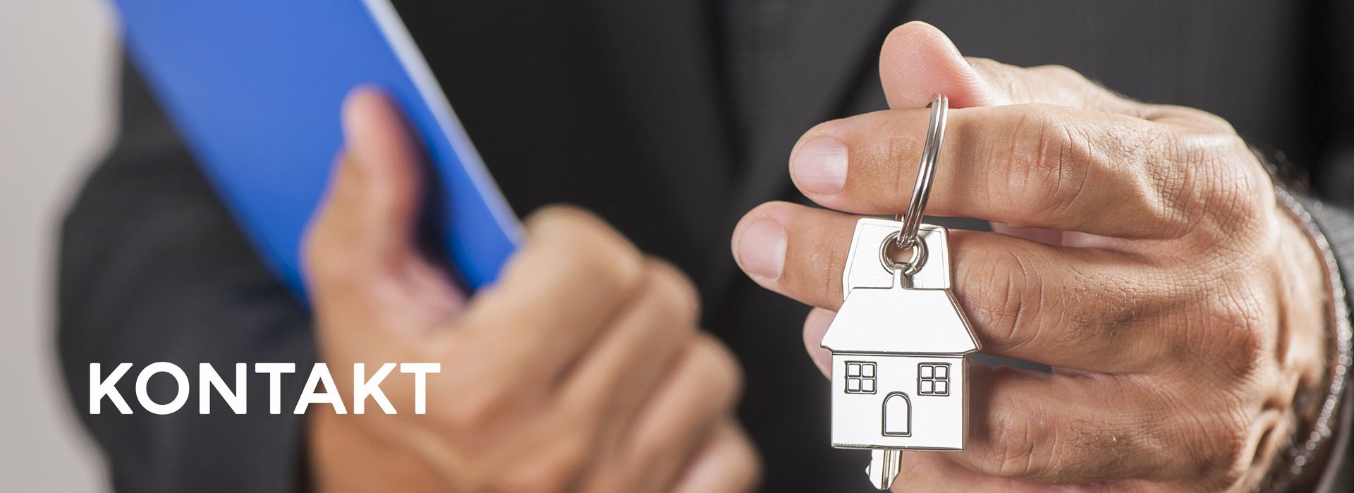 Ein Mann im Anzug hält einen Schlüssel mit einem Haus darauf.