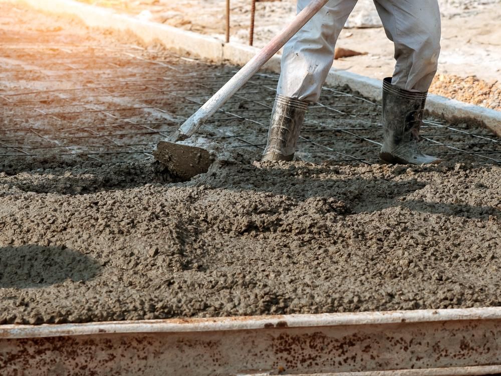 A Man is Spreading Concrete on the Ground With a Shovel — Chooks Sand And Gravel In Moranbah, QLD