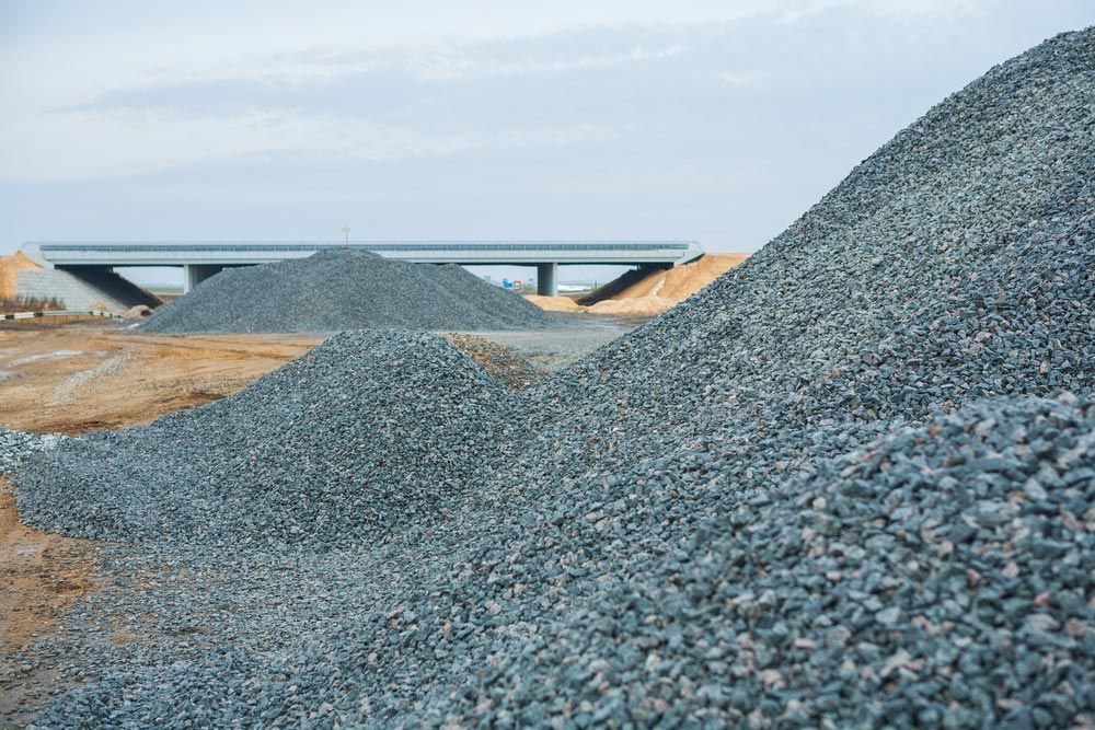 Piles of Gravel at A Construction Site with A Bridge and Cloudy Sky in The Background — Chooks Sand And Gravel In Moranbah, QLD