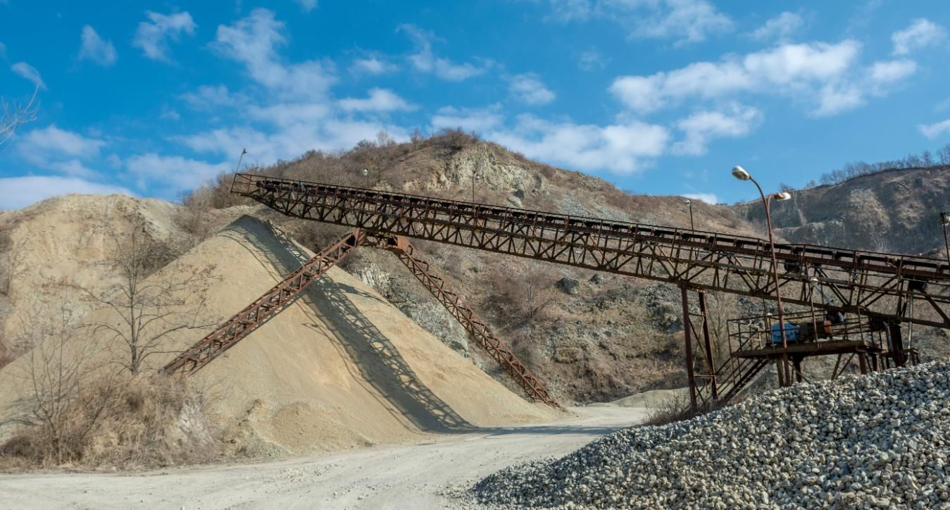 A Conveyor Belt is Moving Gravel in a Quarry With Mountains in the Background — Chooks Sand And Gravel In Paget, QLD
