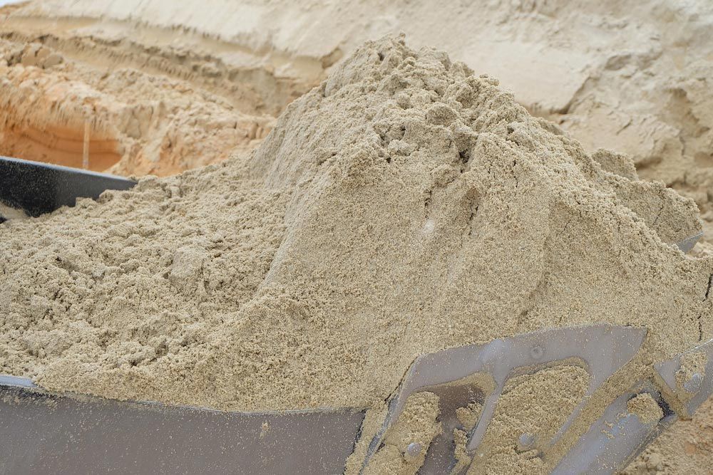 Pile of Beige Sand in A Metal Scoop, with More Sand Piled in The Background — Chooks Sand And Gravel In Bowen, QLD