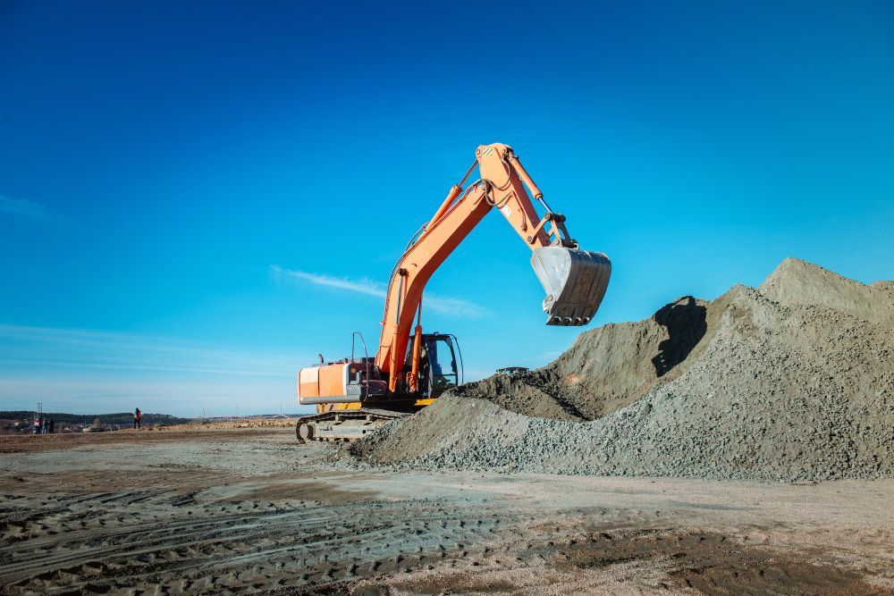 Orange Excavator Loading a Pile of Gravel Against a Bright Blue Sky — Chooks Sand And Gravel In Proserpine, QLD