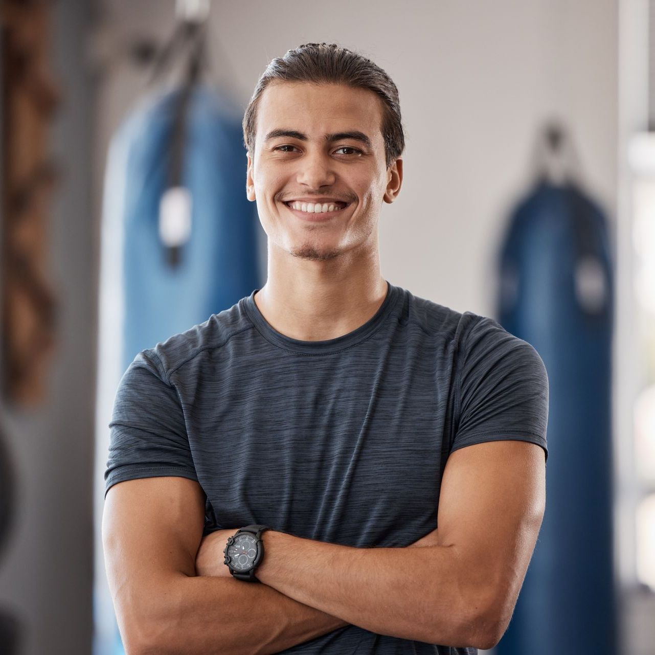 A man is smiling with his arms crossed in a gym.