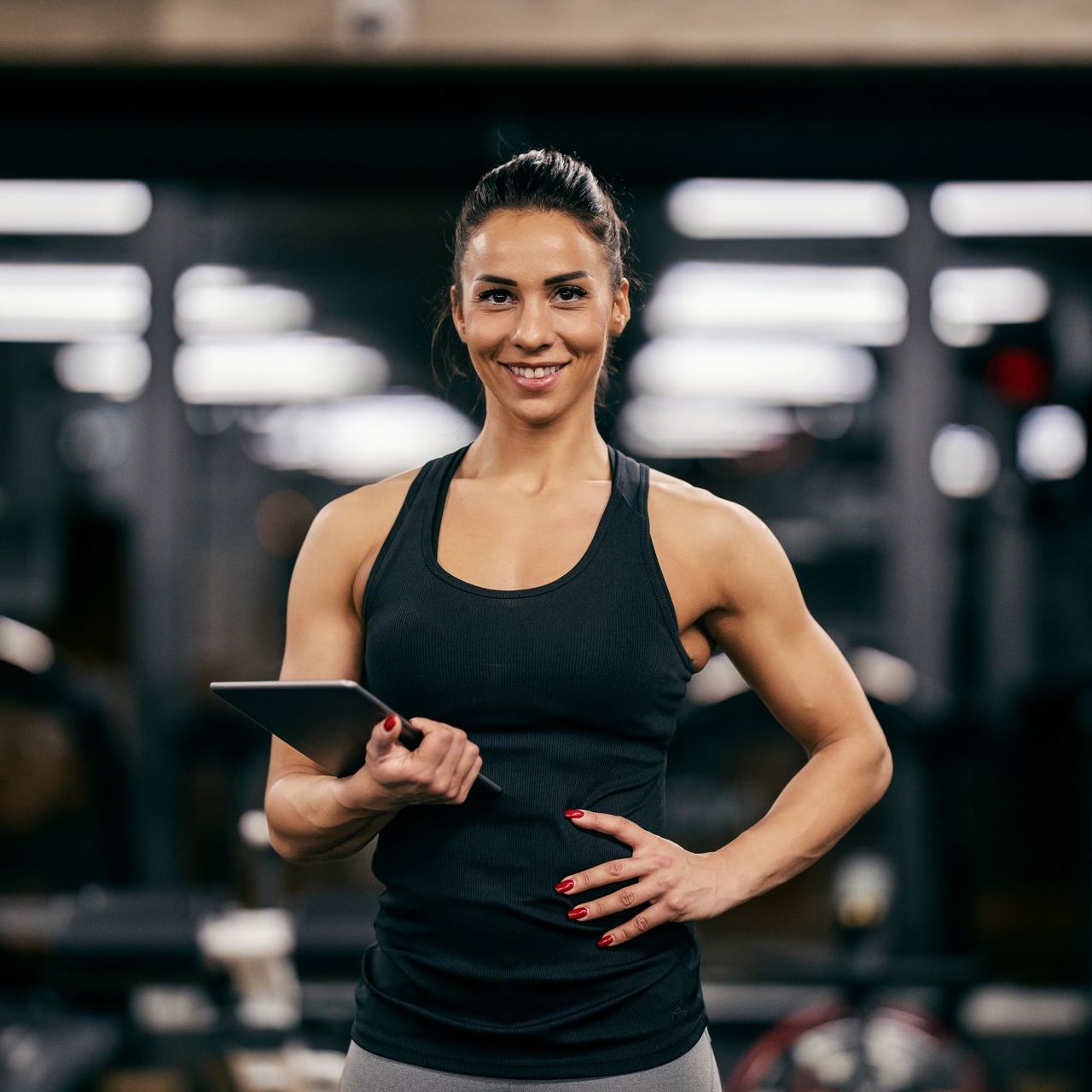 A woman is holding a tablet in a gym and smiling.