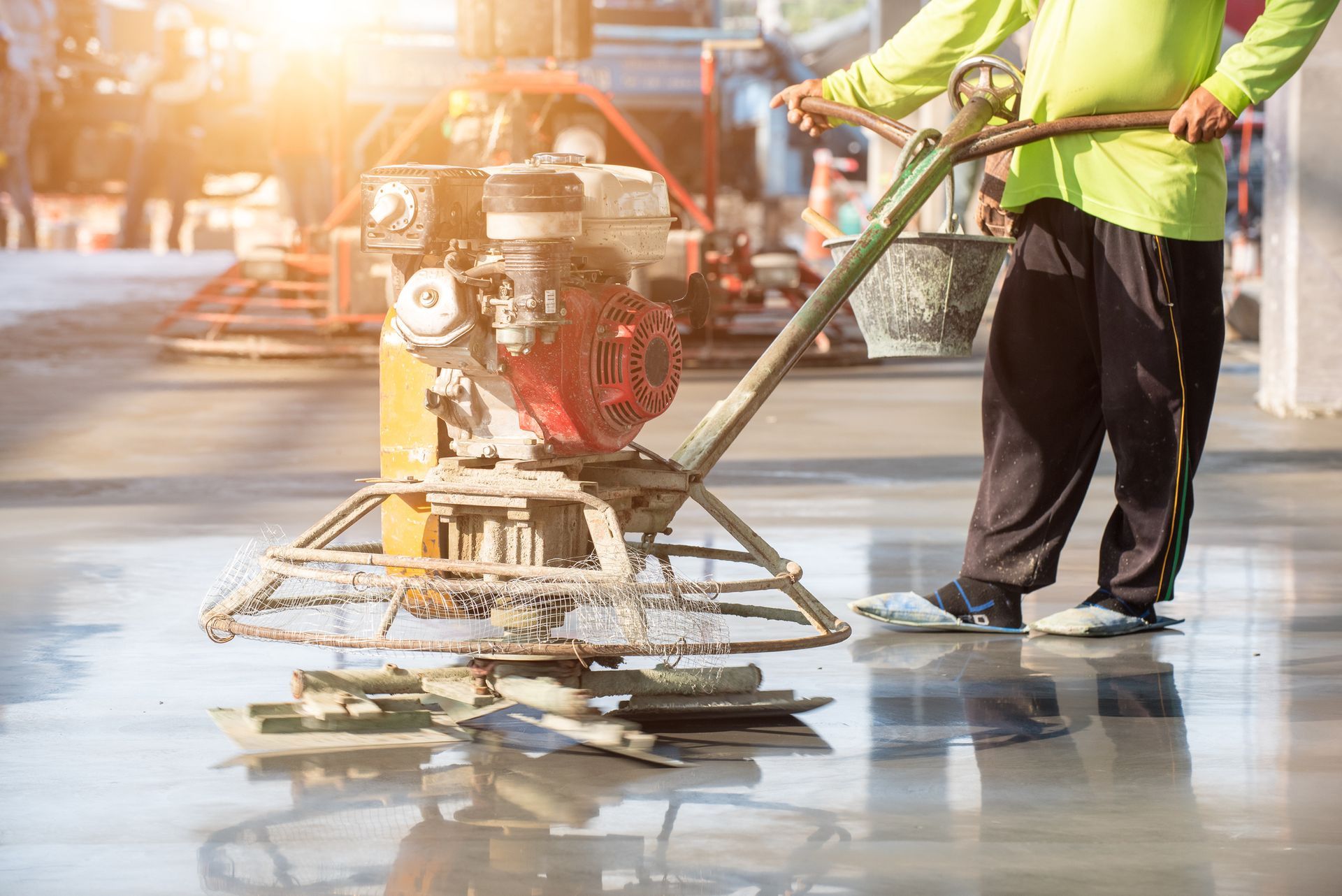 Worker smoothing concrete surface using power trowel during concrete pumping services.