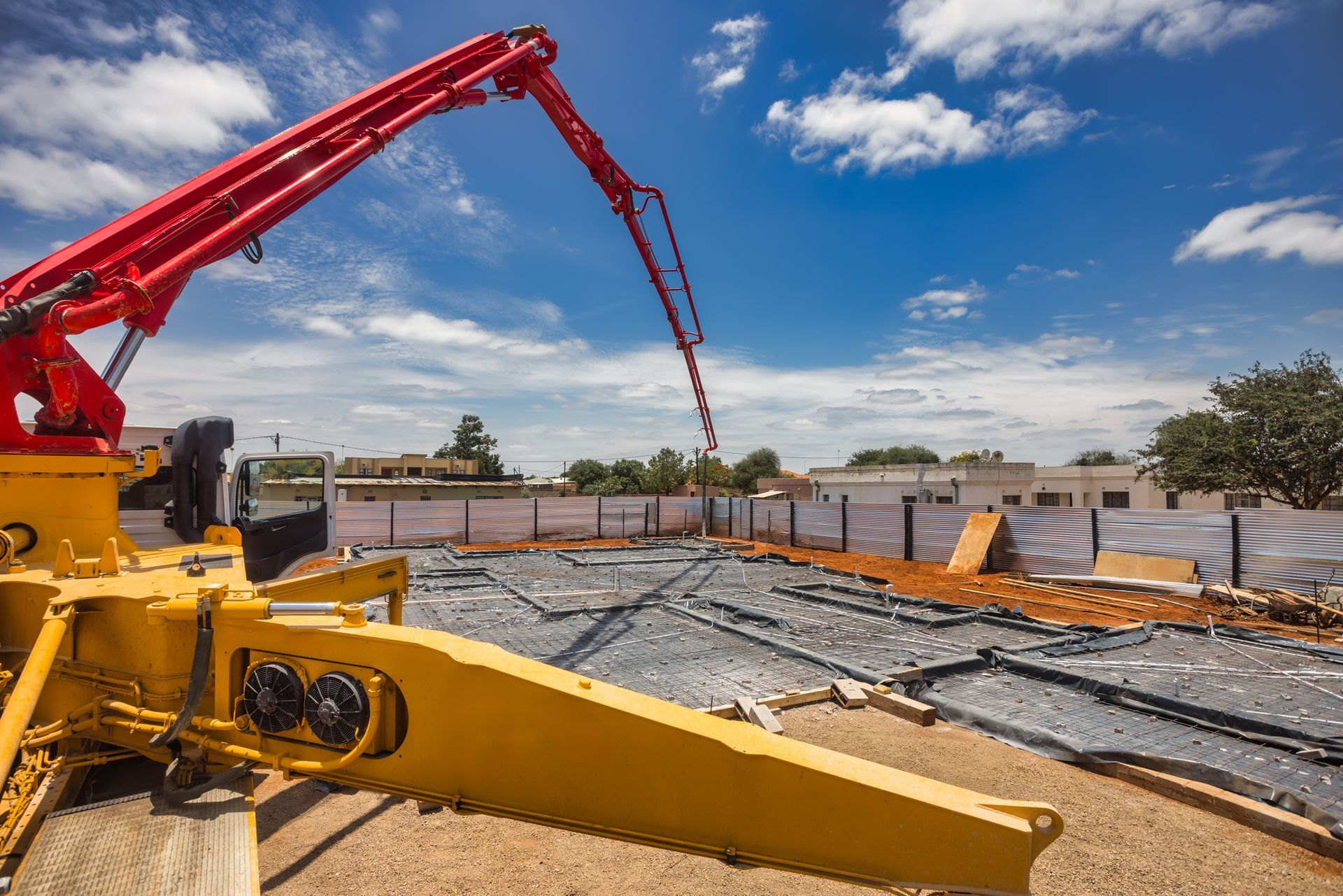 Red and yellow concrete pump extends boom over site prepared for pouring foundation. Red and yellow concrete pump extends boom over site prepared for pouring foundation.