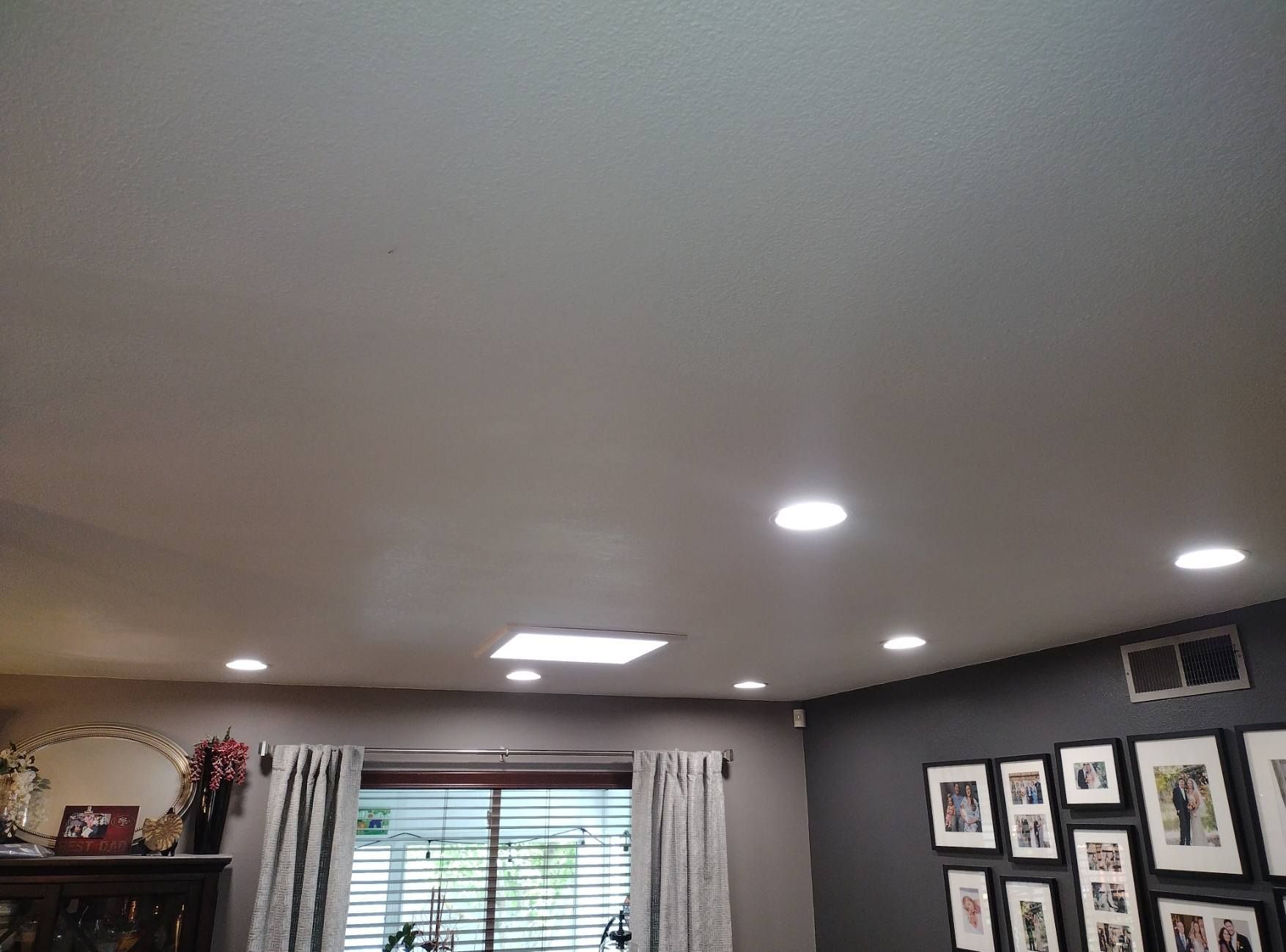 A man wearing a mask is using a drill to install a fire alarm.