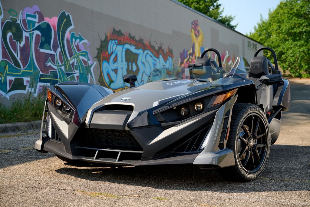 A slingshot is parked in front of a graffiti covered wall.