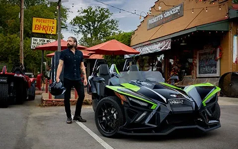 A man is standing next to a slingshot parked in front of a restaurant.