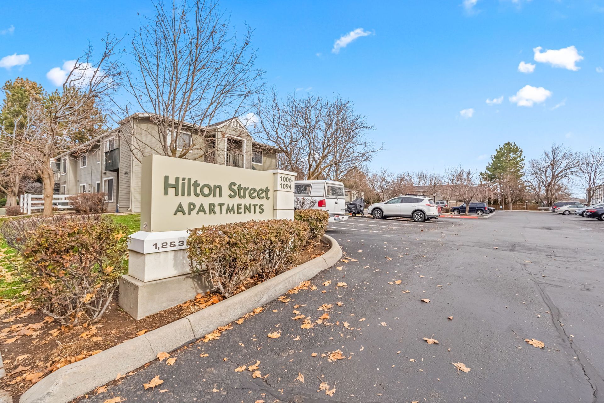 Sign for Hilton Street Apartments with parked cars and building in the background.