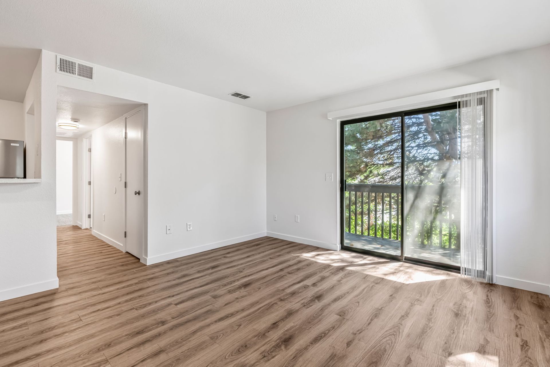 Empty living room with wood-look flooring, white walls, and a sliding glass door to a balcony.