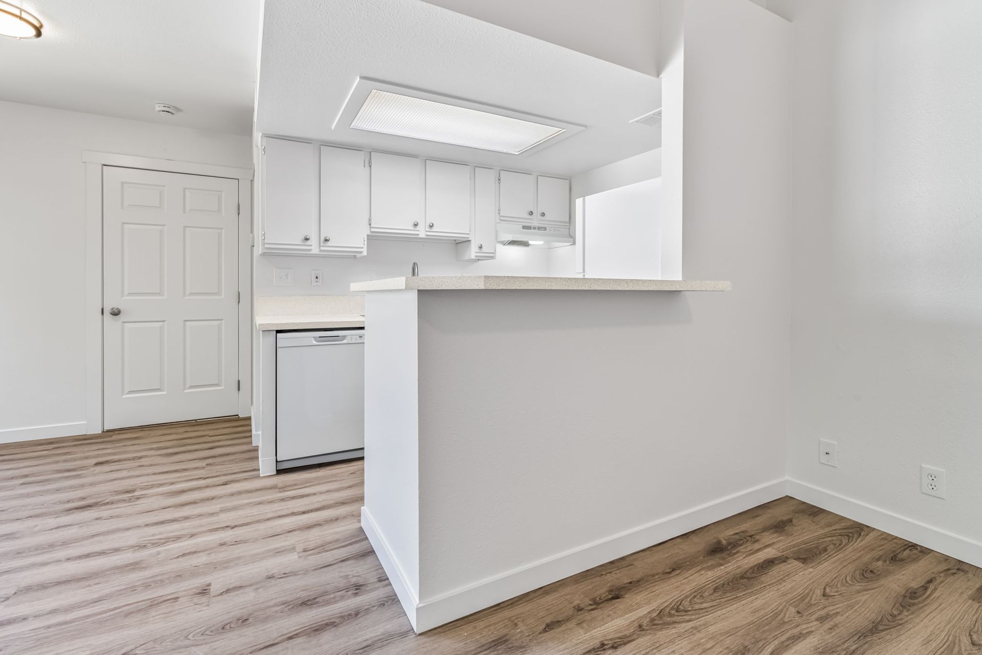 White kitchen with light wood floor, breakfast bar, and white appliances.