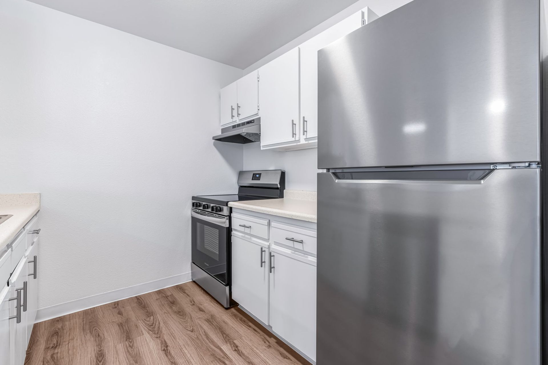 Kitchen with white cabinets, stainless steel appliances, and wood-look flooring.