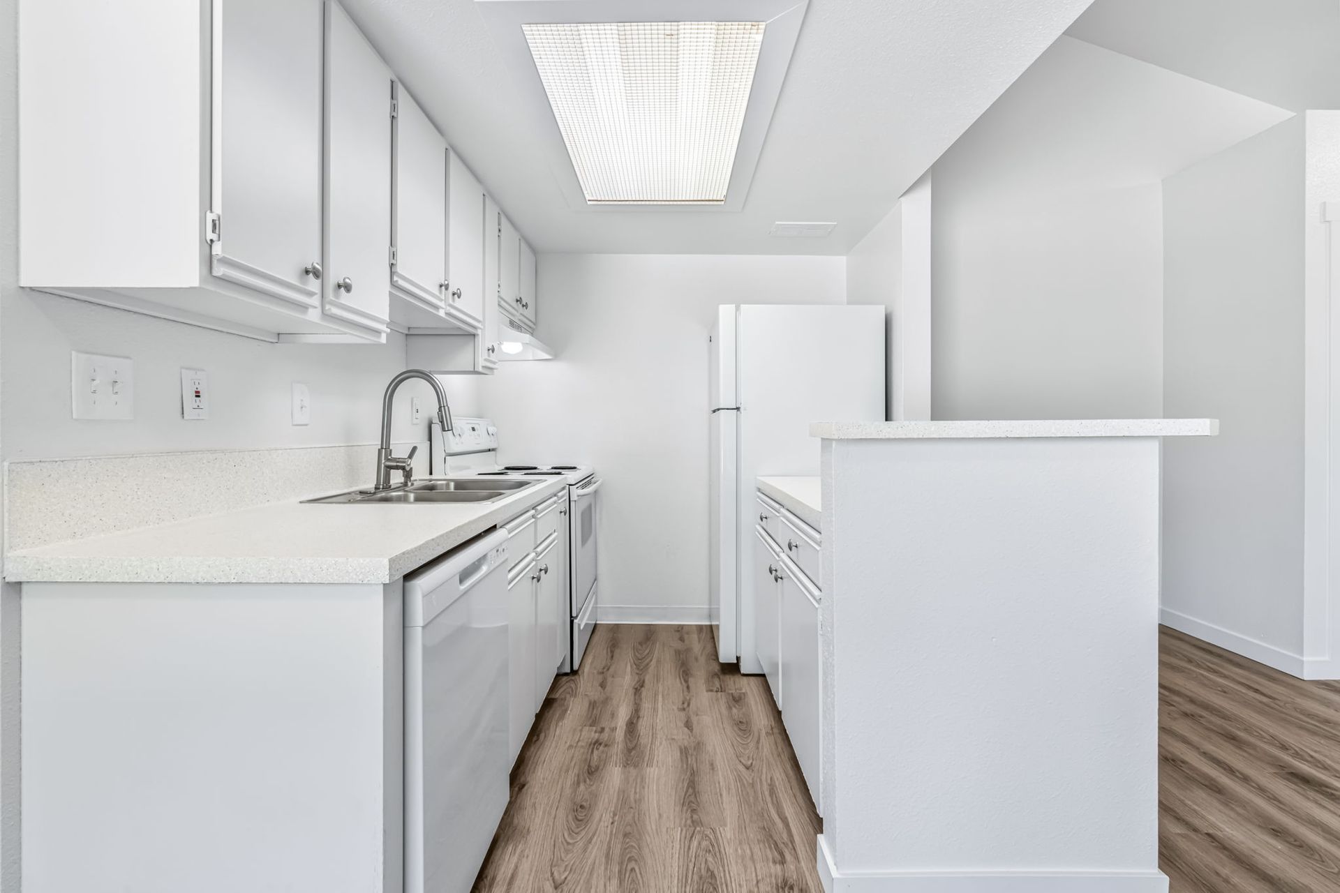 White kitchen with cabinetry, appliances, and countertops; wood-look flooring.