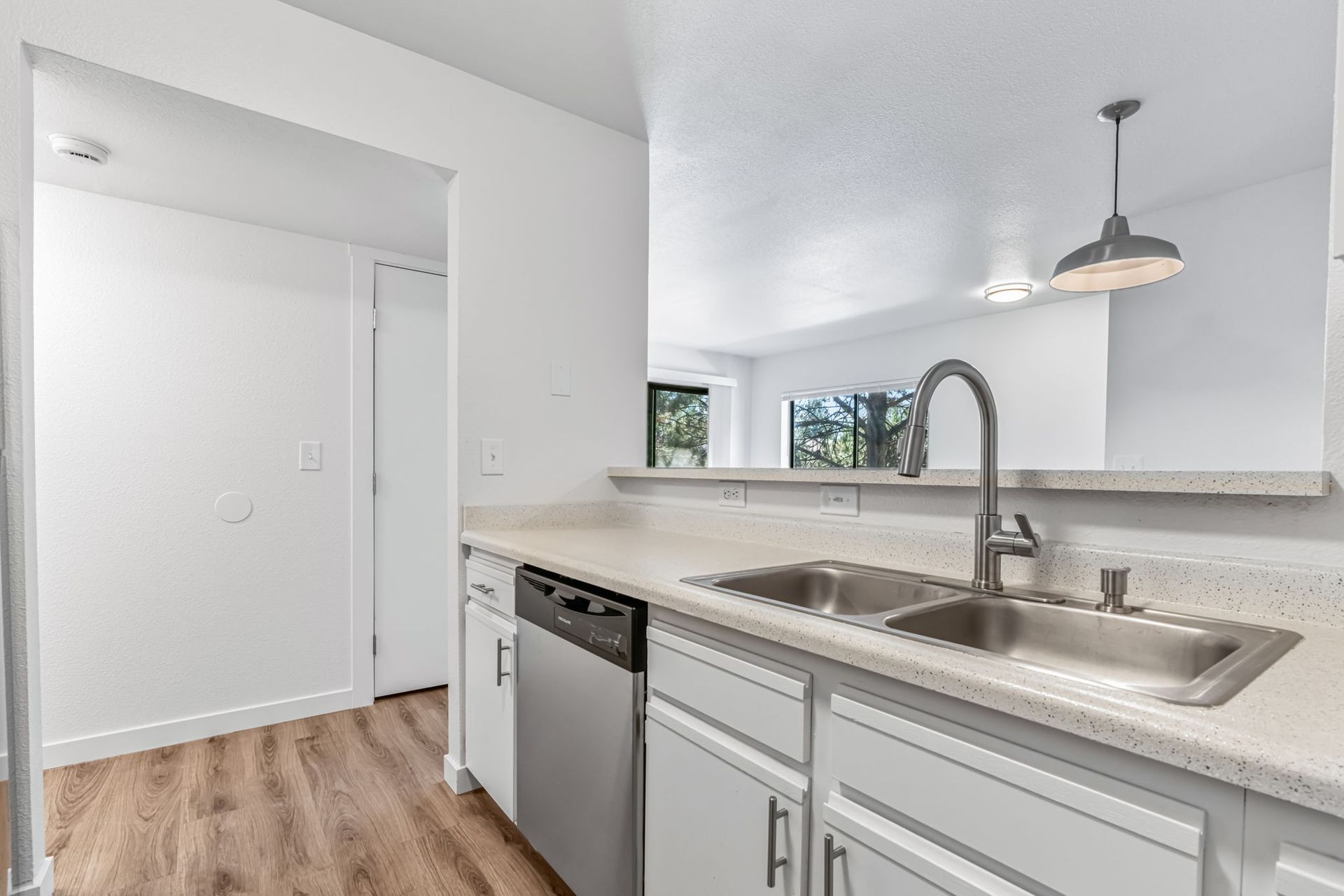 Kitchen with stainless steel sink, dishwasher, white cabinets, and light countertop.