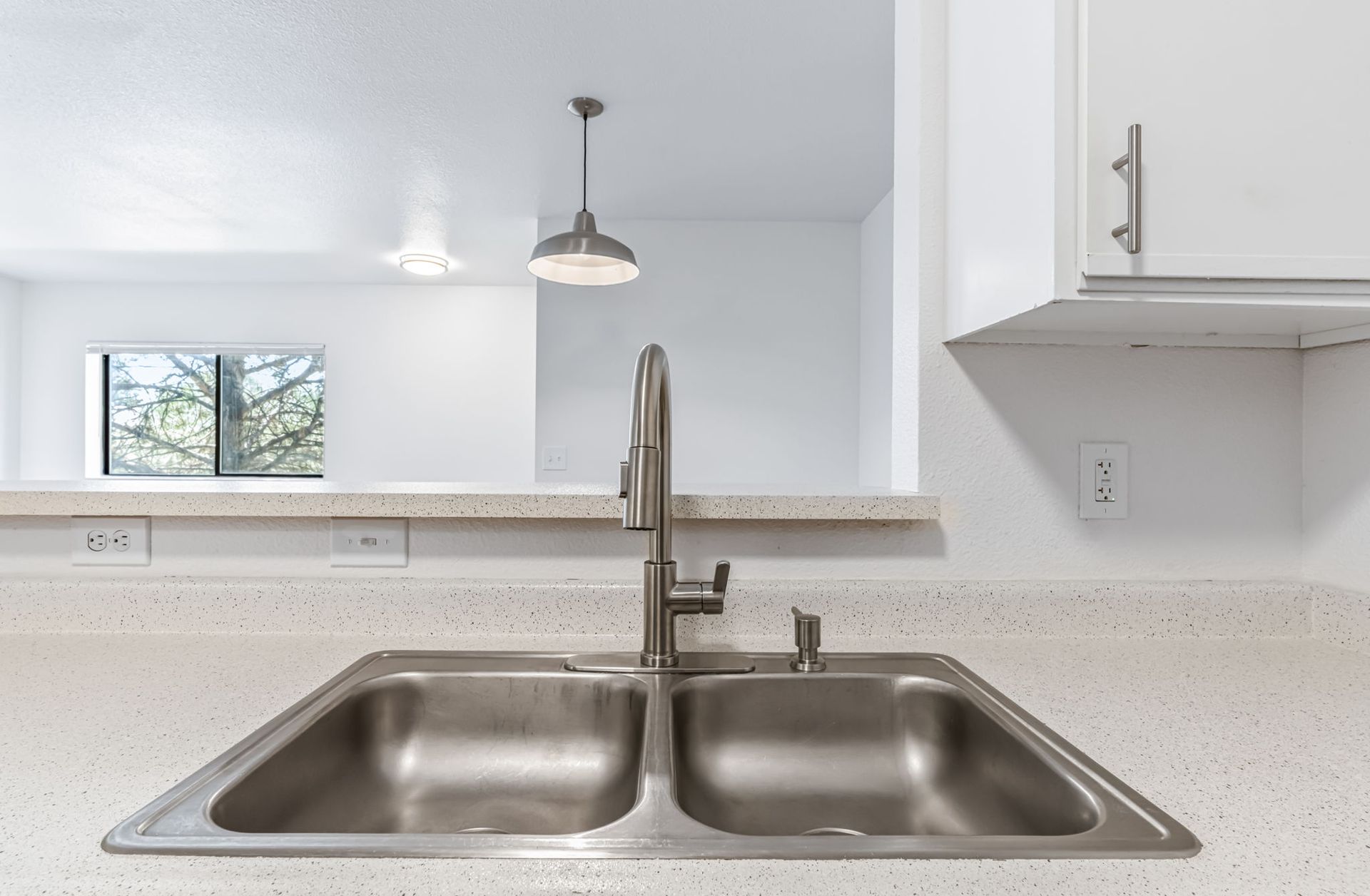 Stainless steel double sink and faucet on a white countertop with a window view in the background.