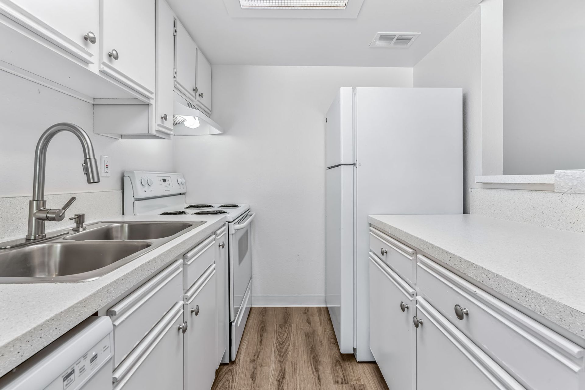 White kitchen with stainless steel sink, appliances, and cabinetry; light wood-look floor.