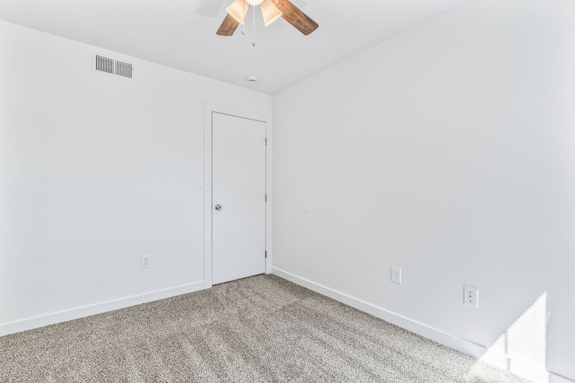 Empty room with white walls, carpeted floor, closed door, ceiling fan.