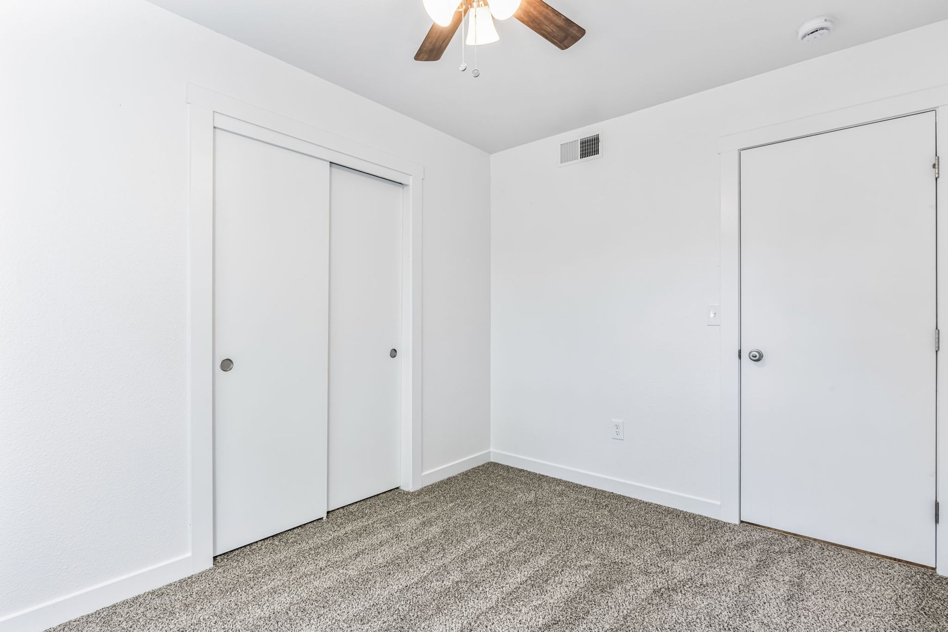Empty bedroom with white walls, sliding closet doors, carpet, and a ceiling fan.