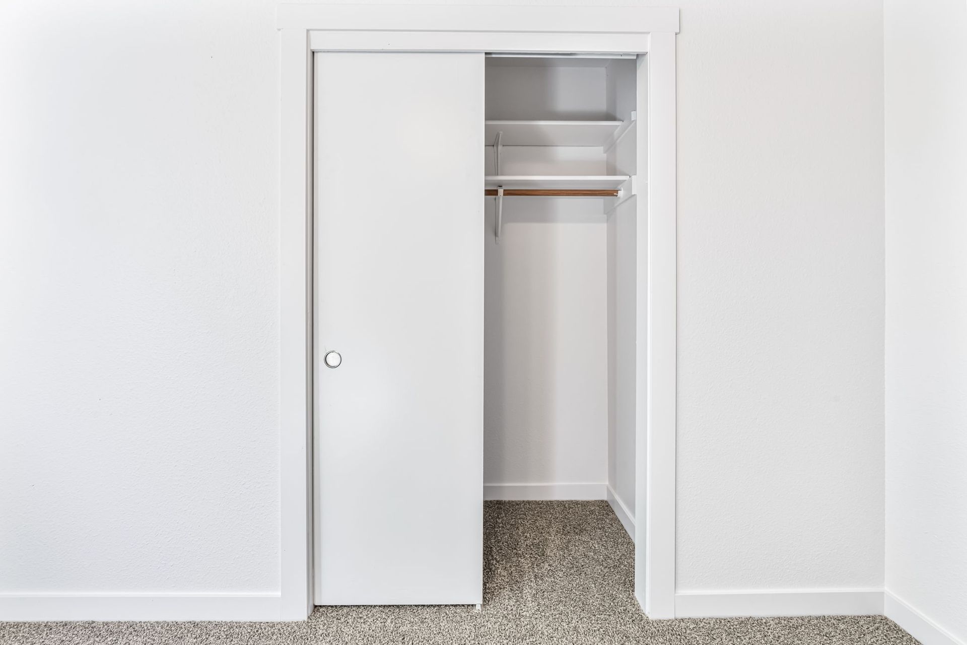 White closet with sliding door partially open, revealing shelving and hanging rod; carpeted floor.