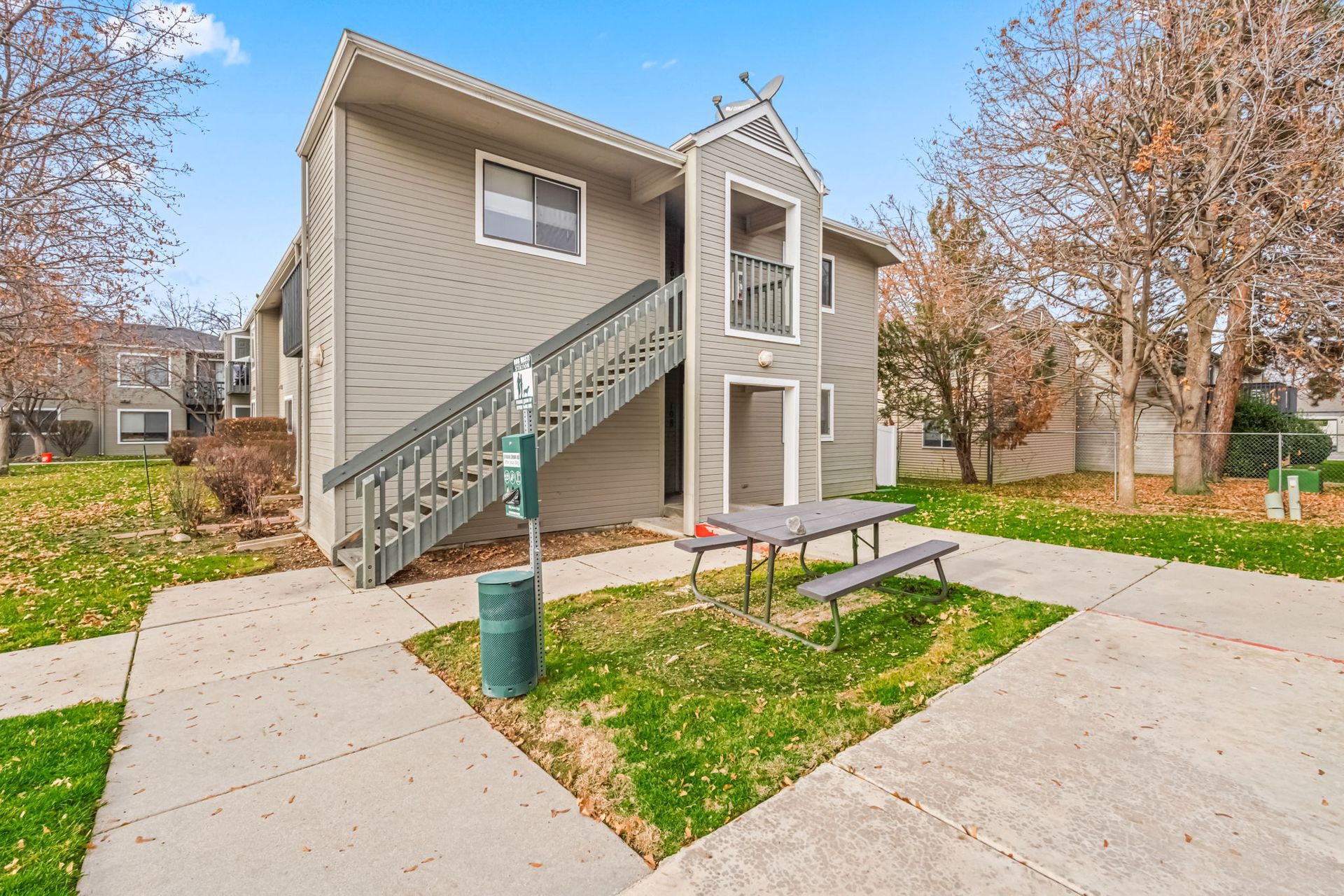 Gray apartment building with outdoor stairs, a picnic table, and grass.