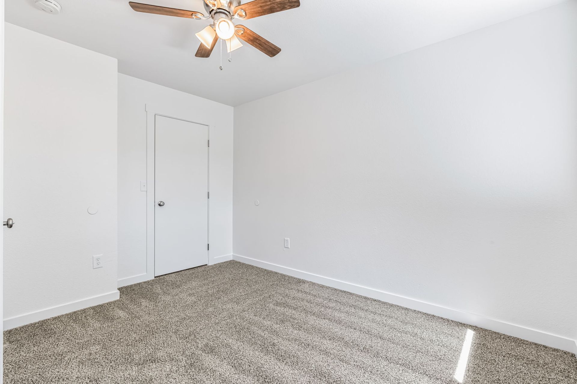 Empty room with white walls, carpet flooring, and a ceiling fan.
