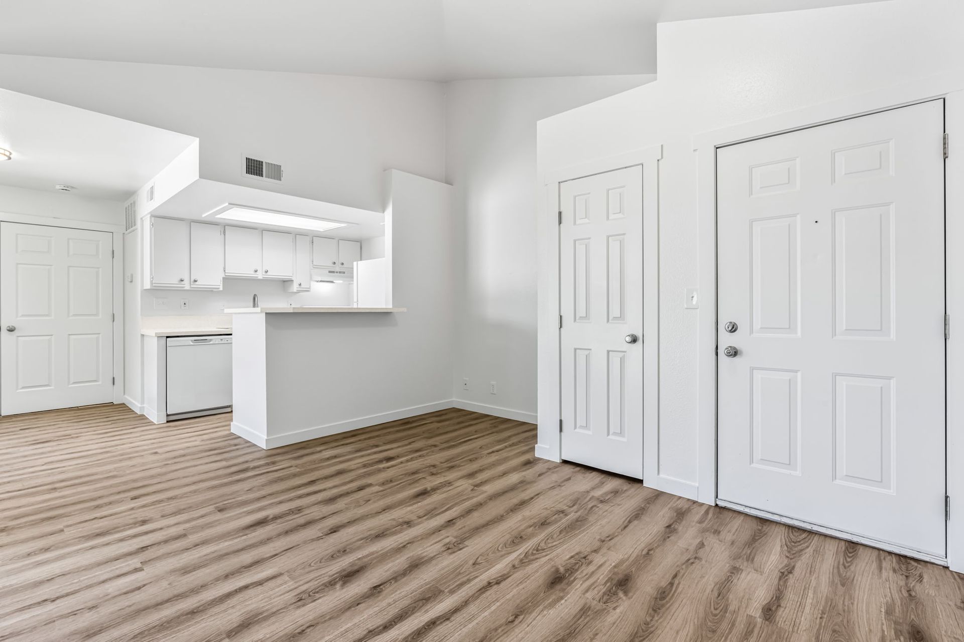 Empty apartment interior, featuring a kitchen and two white doors.