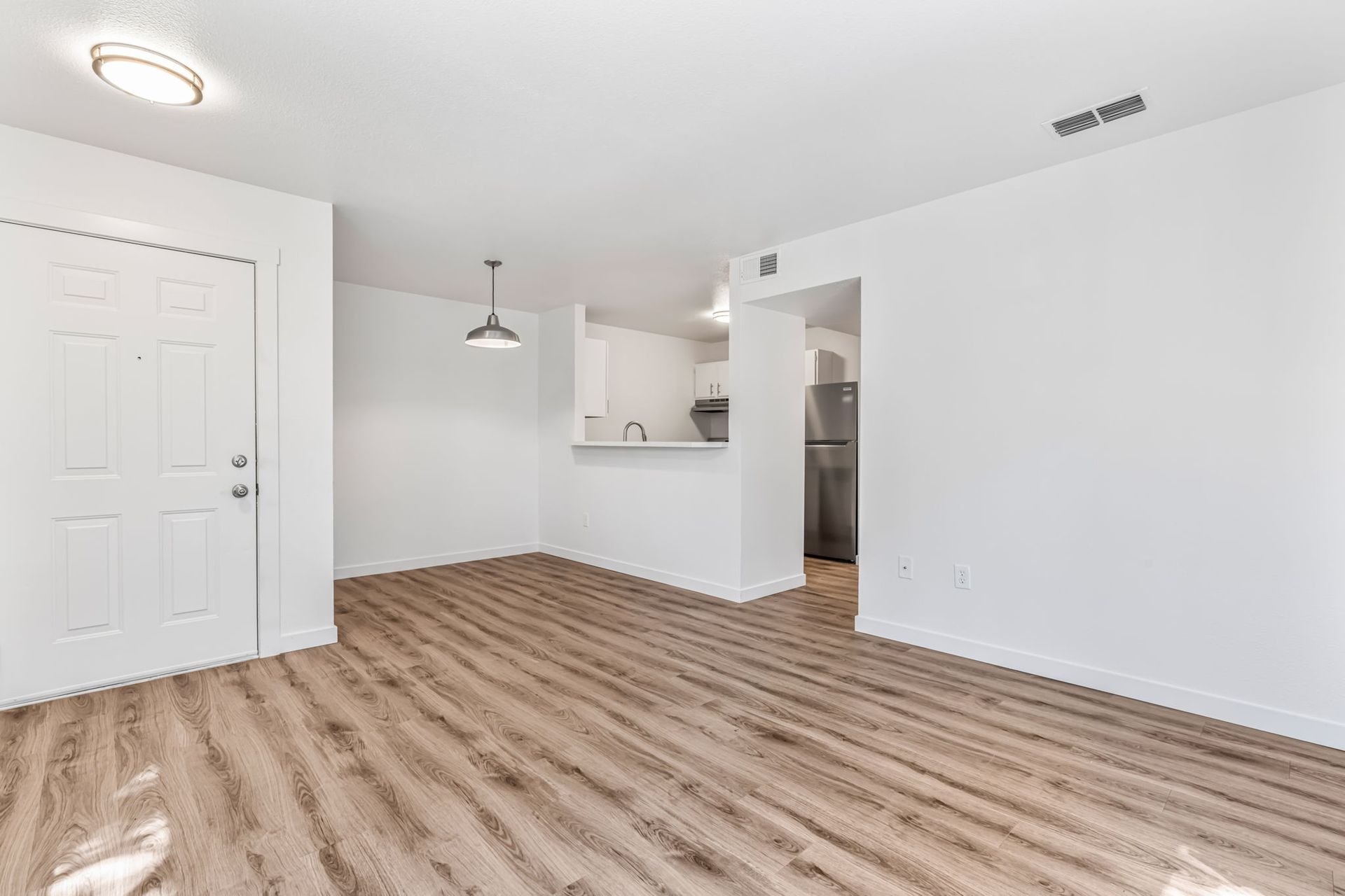 Empty apartment living space with wood flooring and white walls.