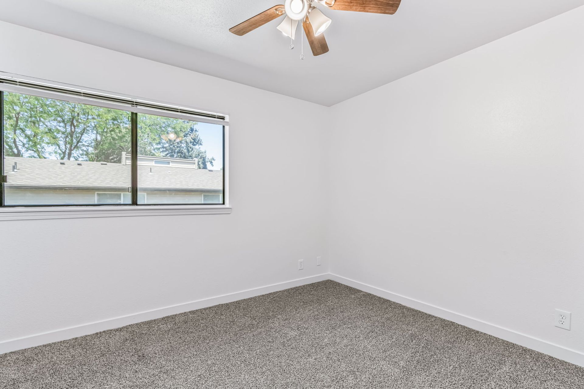 Empty room with a window, white walls, carpet, and a ceiling fan.