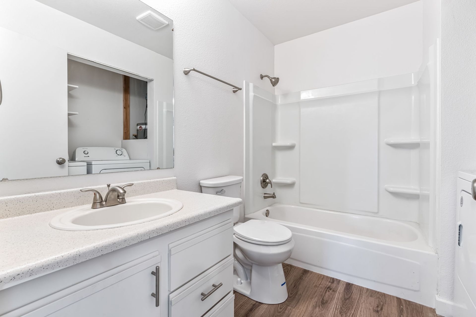 White bathroom with a vanity, toilet, and bathtub/shower combo with wood-look flooring.