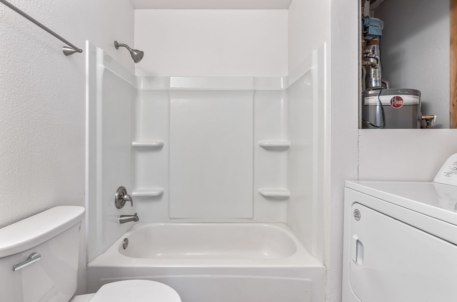 A small, white bathroom with a tub/shower combo, toilet, and washing machine.