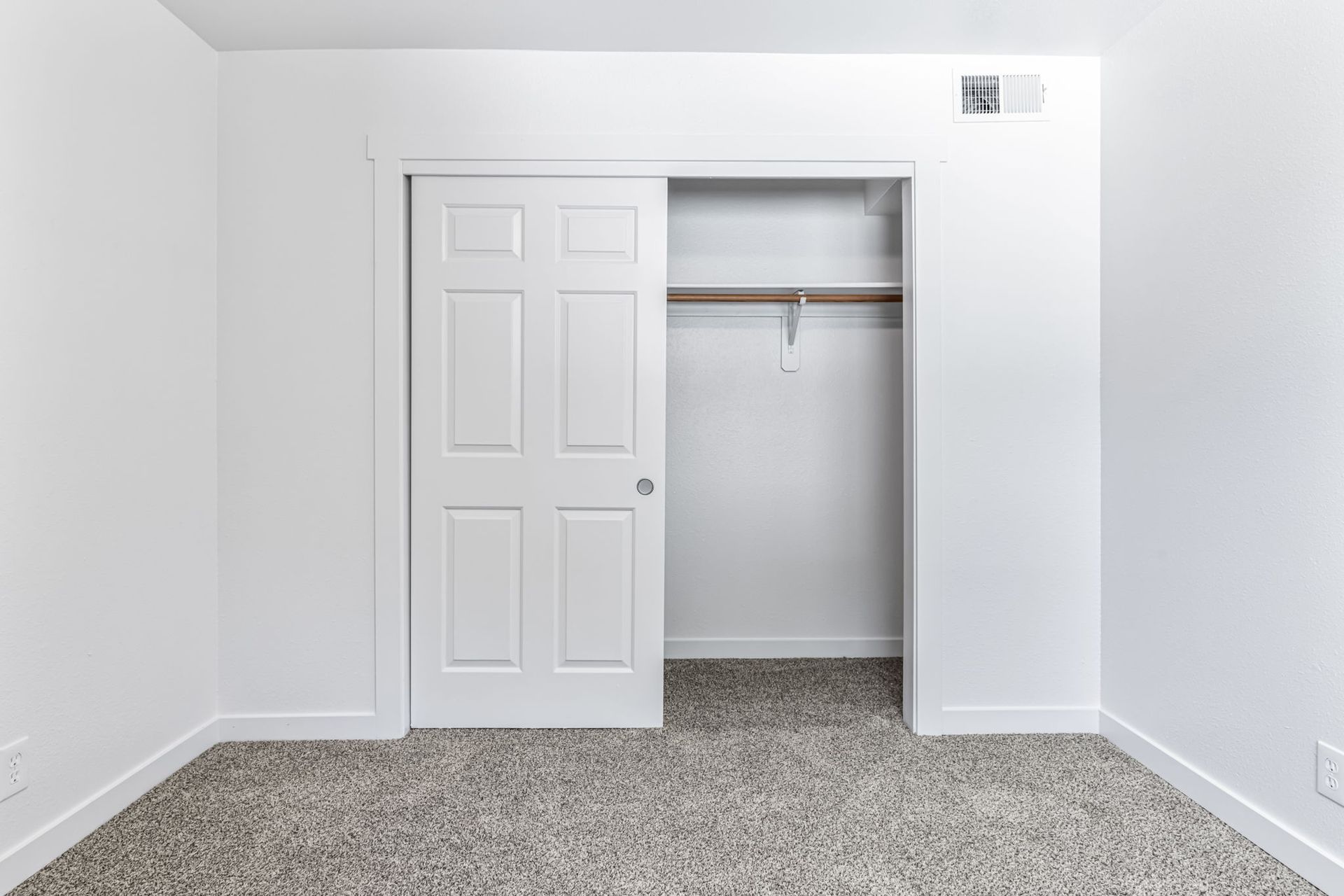 Empty white room with partially open closet and carpeted floor.