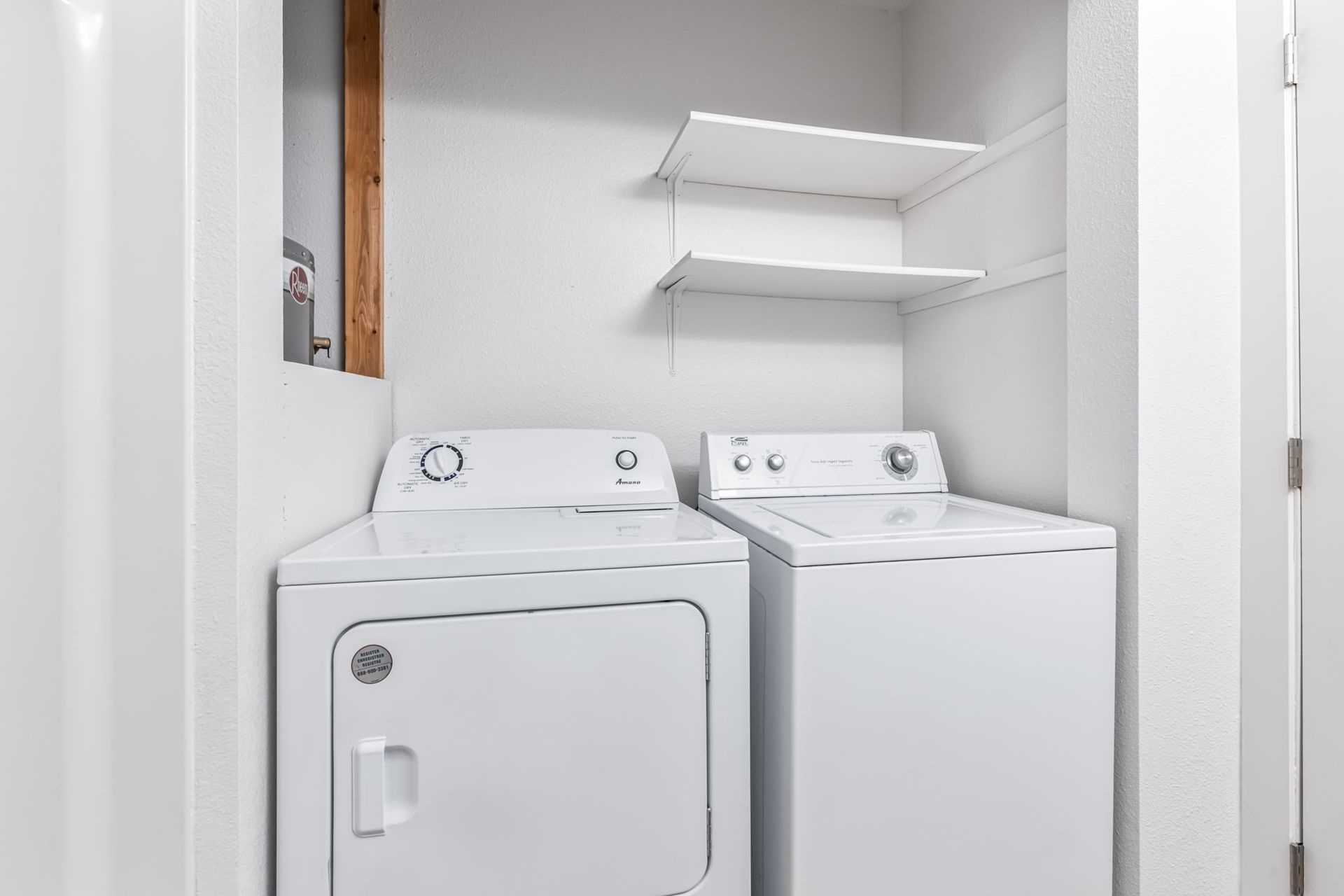 White washer and dryer in a small laundry room with a shelf.