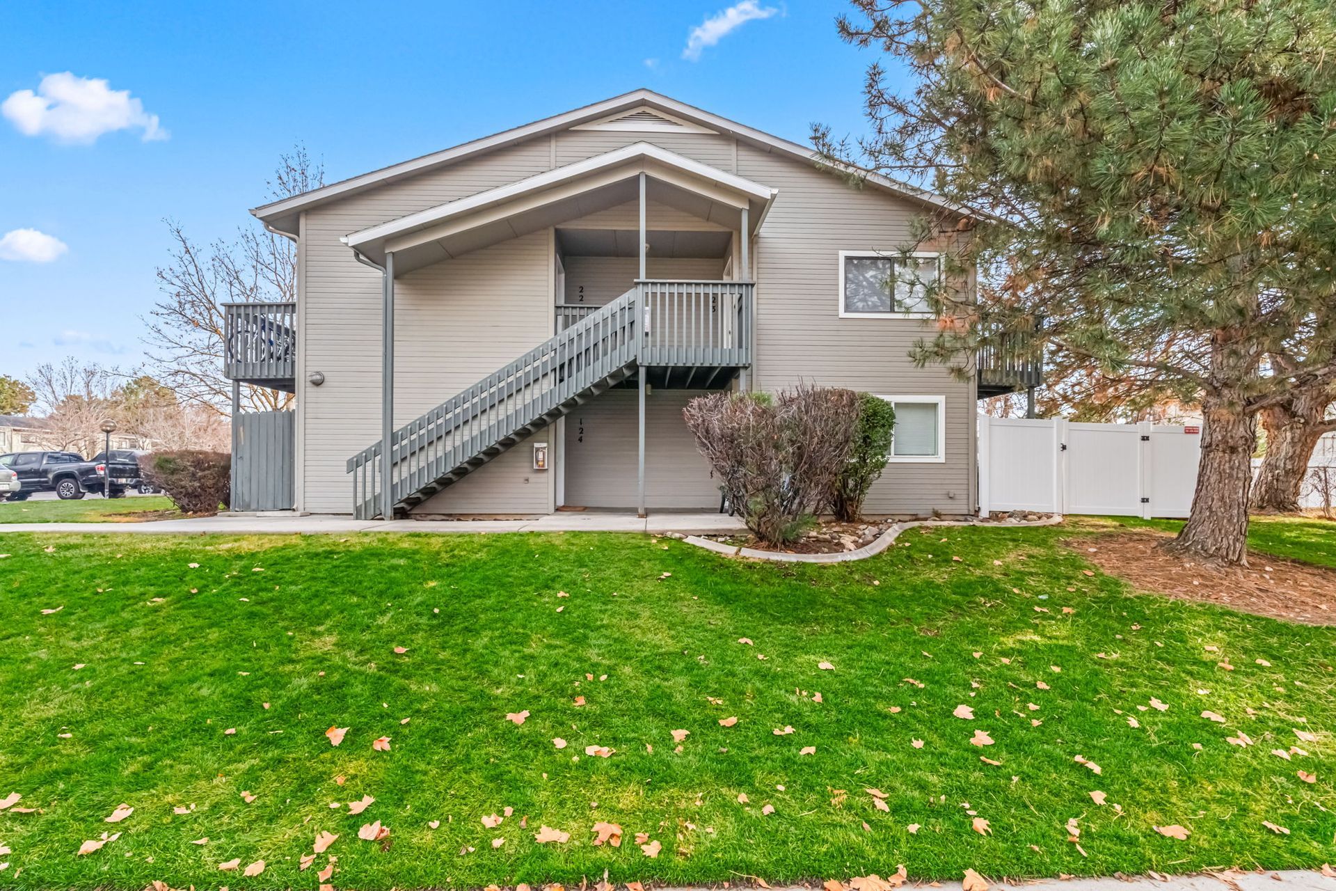 Two-story apartment building with stairs, gray siding, green lawn, and a blue sky.